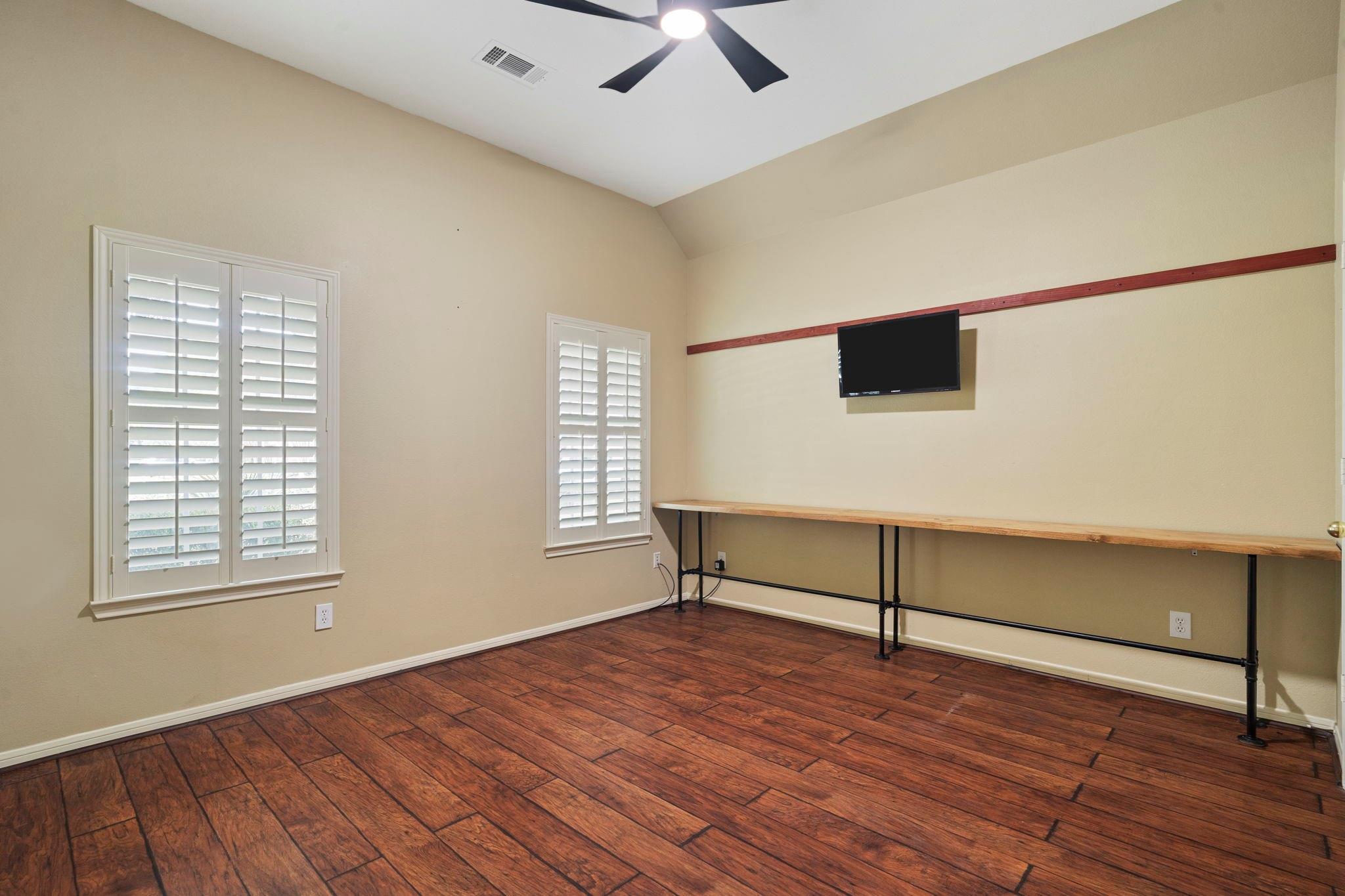 Room with vaulted ceiling, plantation shutters, wood-look flooring, and a long wall counter.