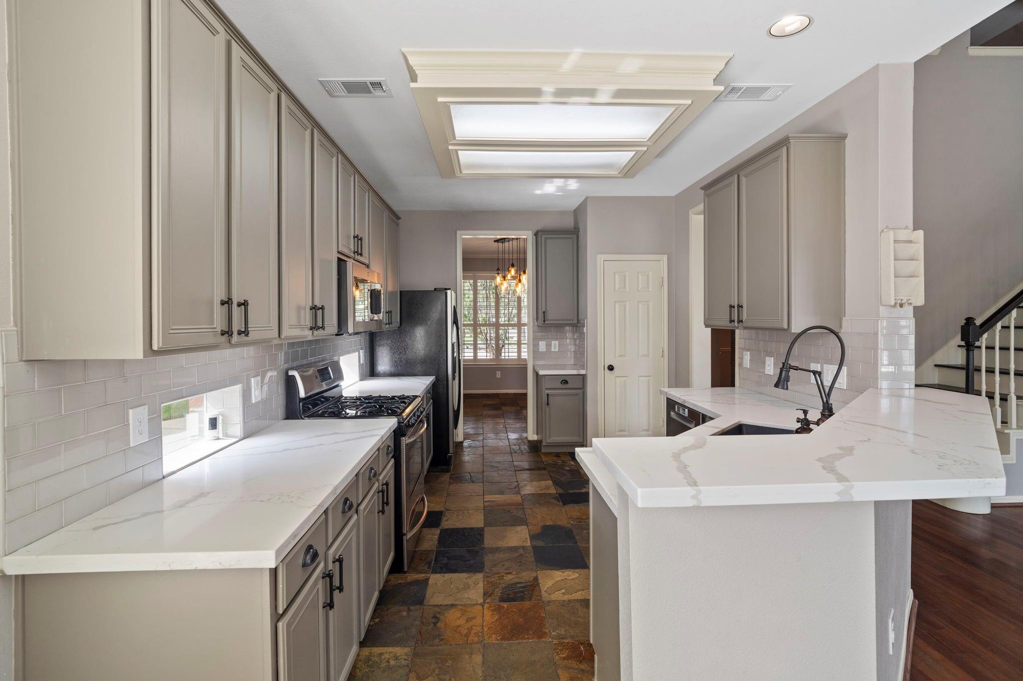 Kitchen with gray cabinets, white stone island, black faucet, skylight, and slate tile flooring.