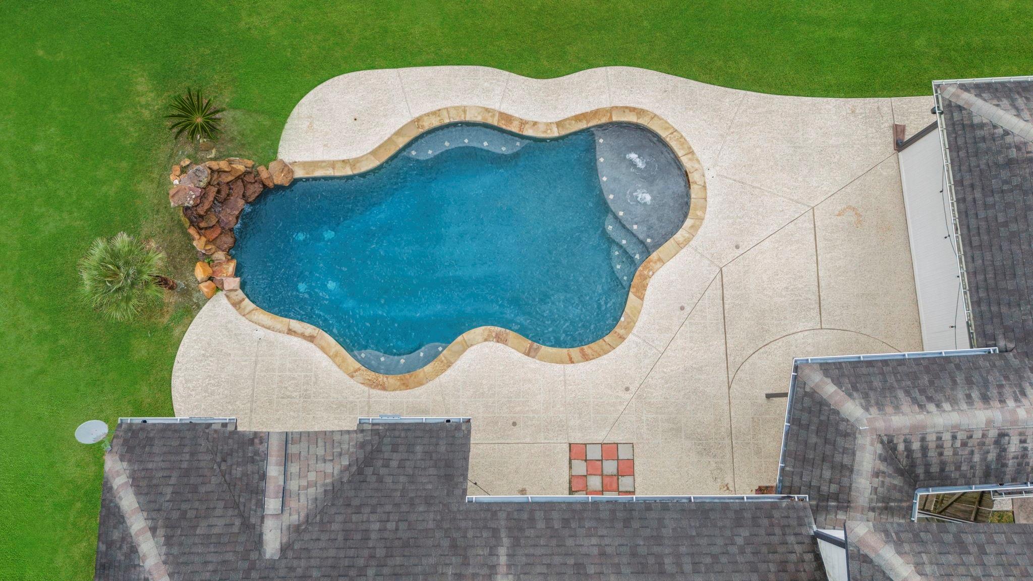 Freeform backyard pool with attached bubbling spa, broad concrete deck, and rock landscaping.