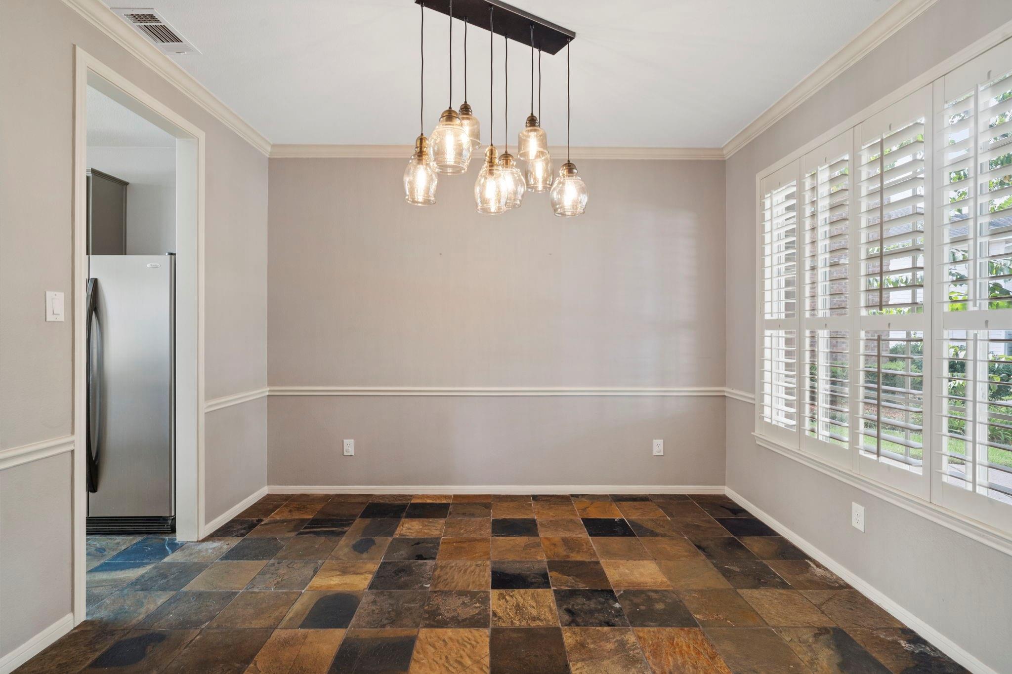 Unfurnished dining area with slate tile floors, glass pendant lights, and plantation shutters.