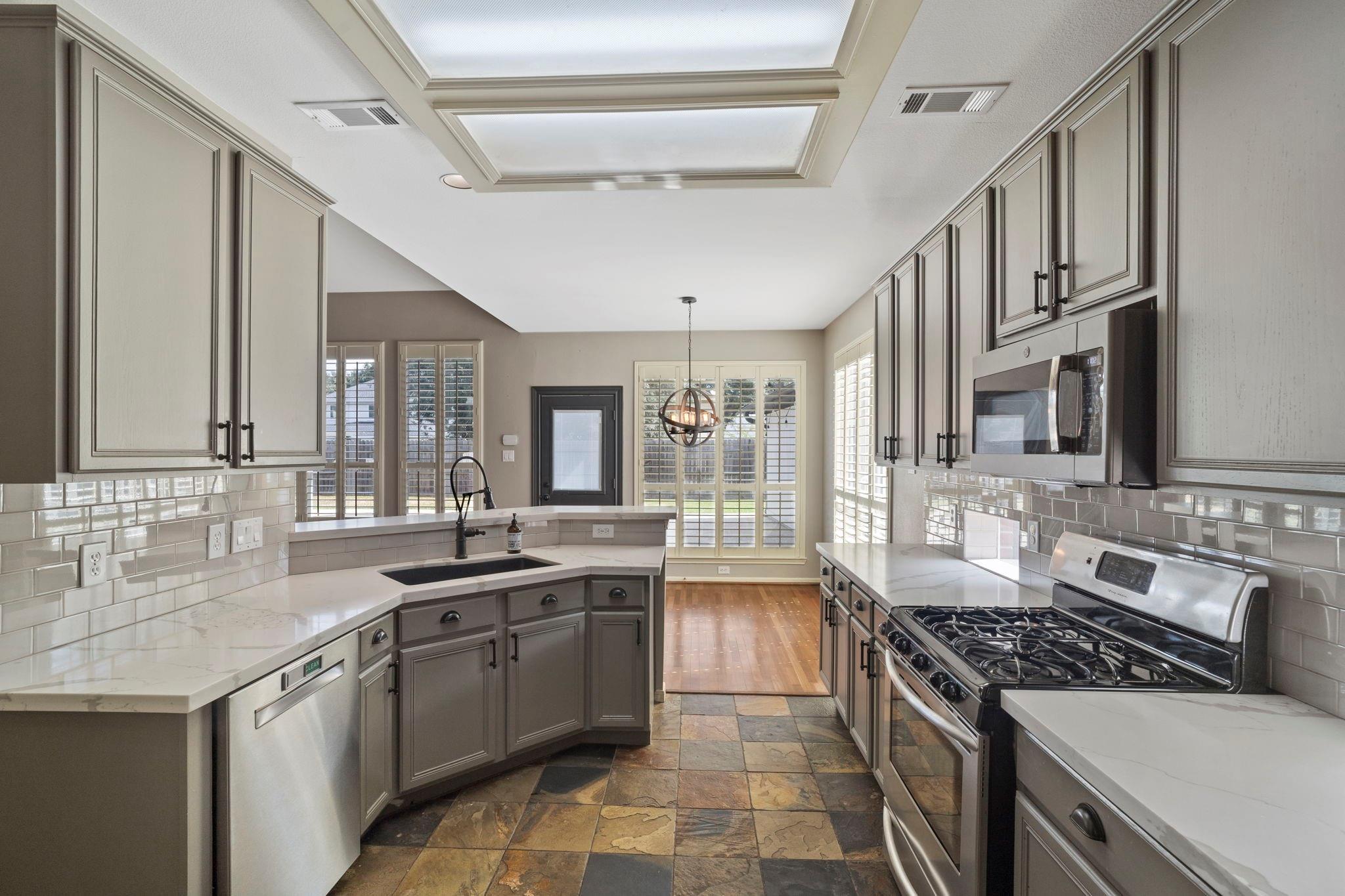 Kitchen with gray cabinets, white countertops, stainless appliances, and a peninsula sink.
