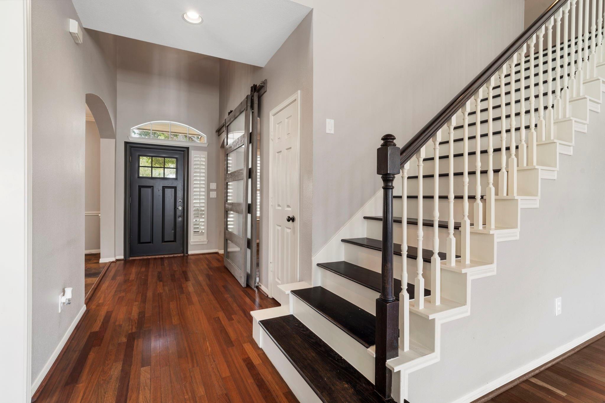 Entry foyer with hardwood floors, black front door, and staircase with dark treads and white balusters.