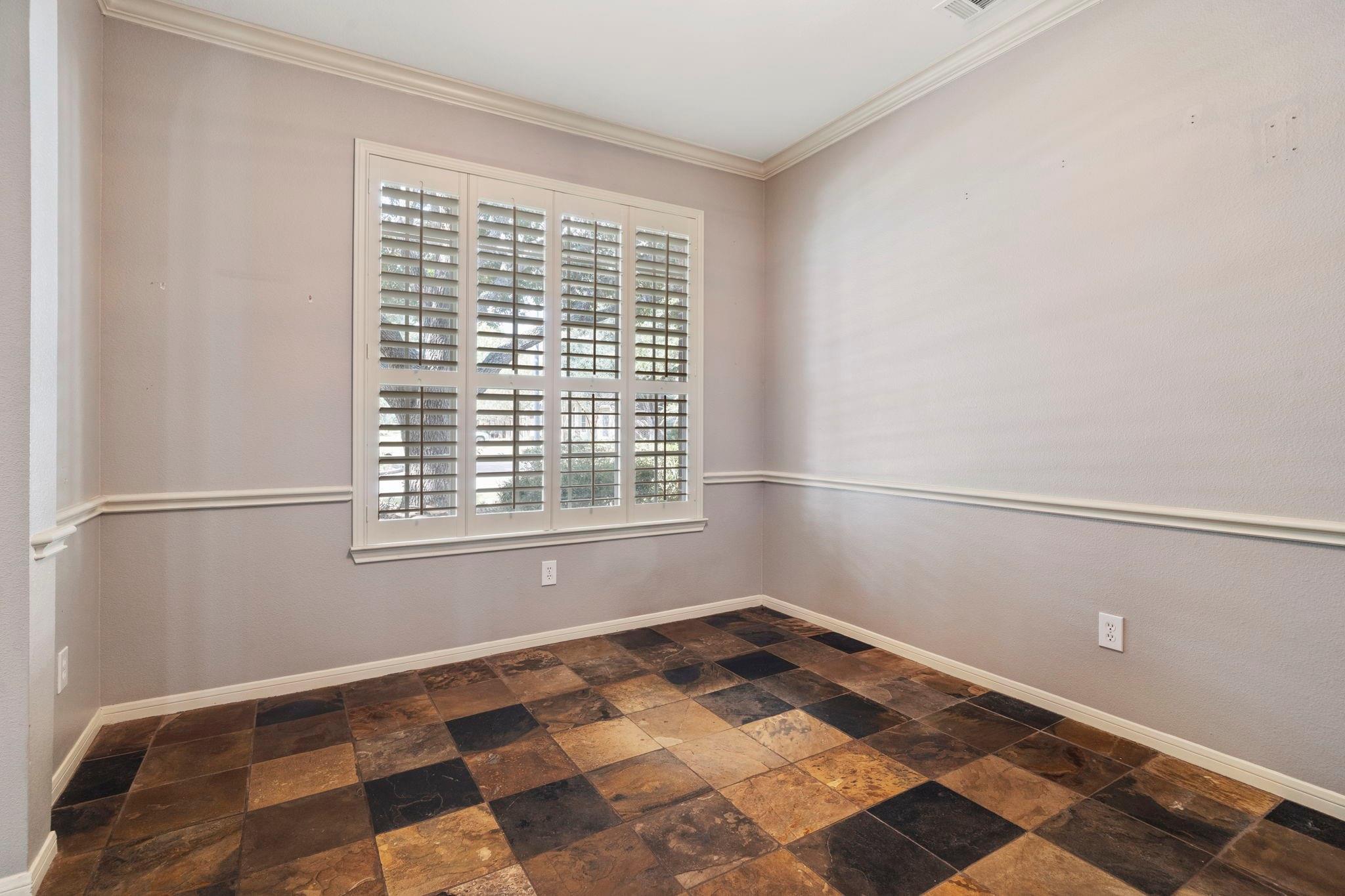 Empty room with plantation-shuttered window and multicolored stone-tile floor.