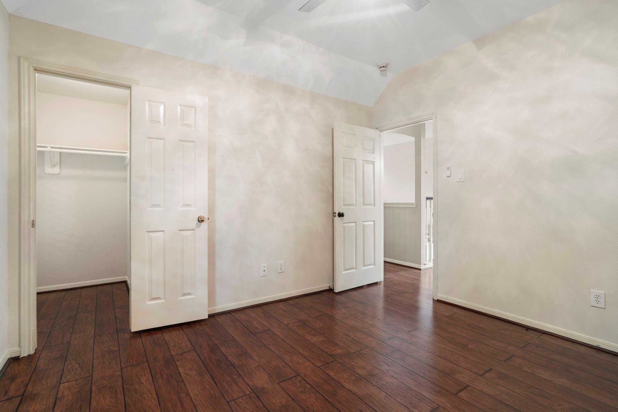 Empty bedroom with dark plank flooring, an open closet, and a high angled ceiling.