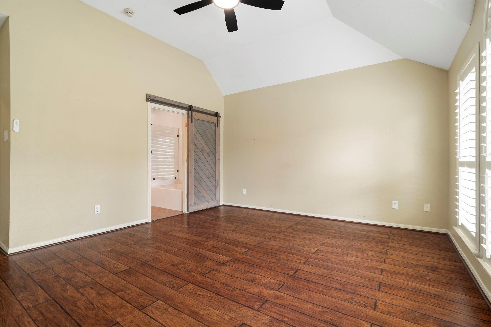 Empty room with vaulted ceiling, dark plank flooring, plantation shutters, and a sliding barn door.