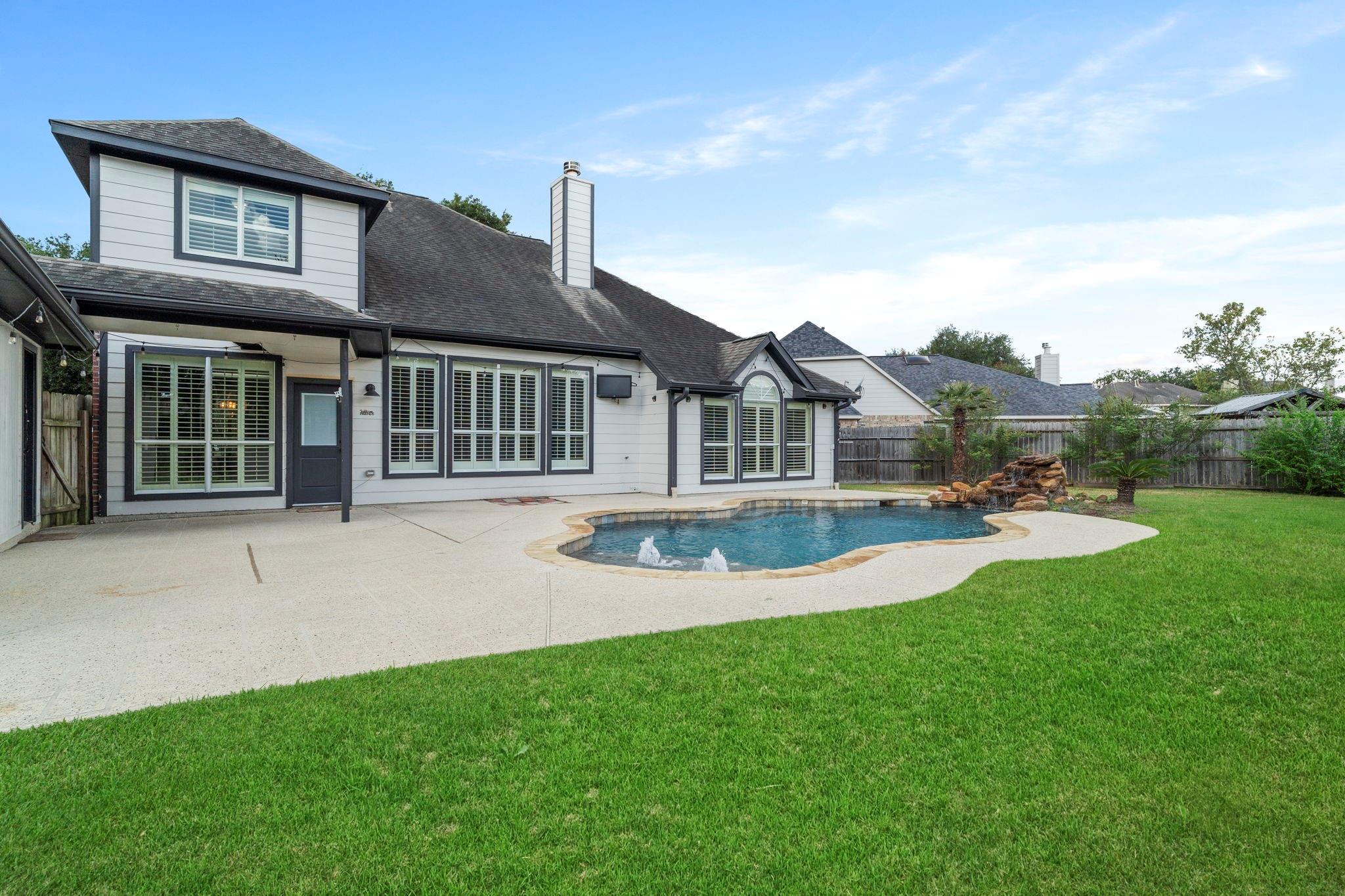 Rear of a gray two-story home with a freeform pool, fountains, and a broad lawn.