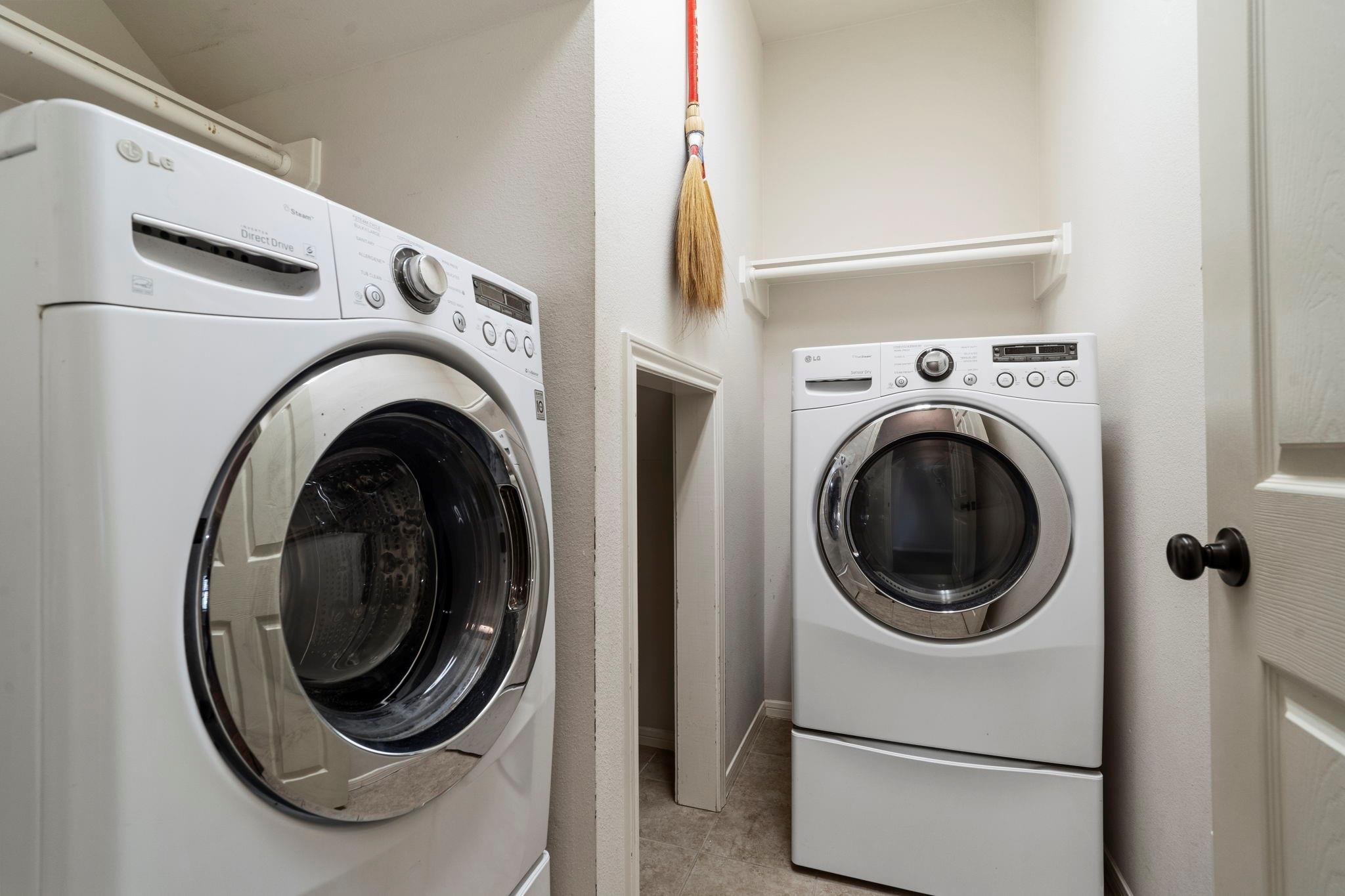 Laundry room with two white front-loading machines and a high wall shelf.