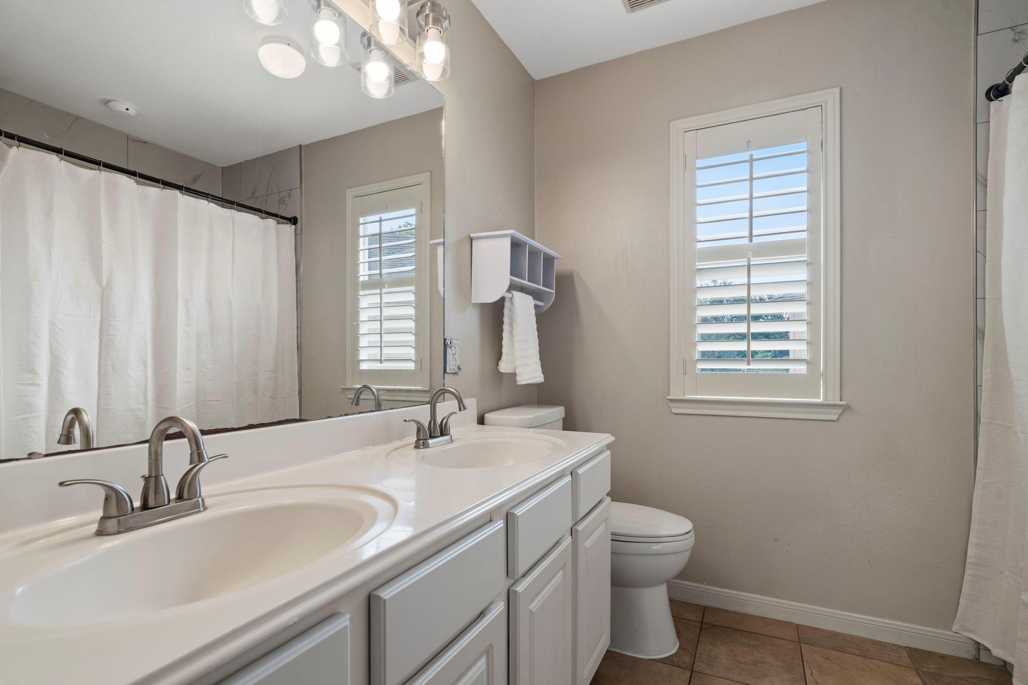 Bathroom with a double-sink vanity, large mirror, shuttered window, and curtained tub or shower.