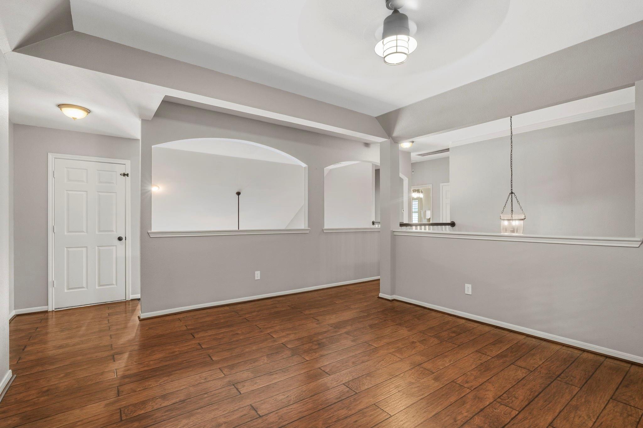 Empty dining area with wood flooring, arched pass-throughs, and a hanging pendant light.