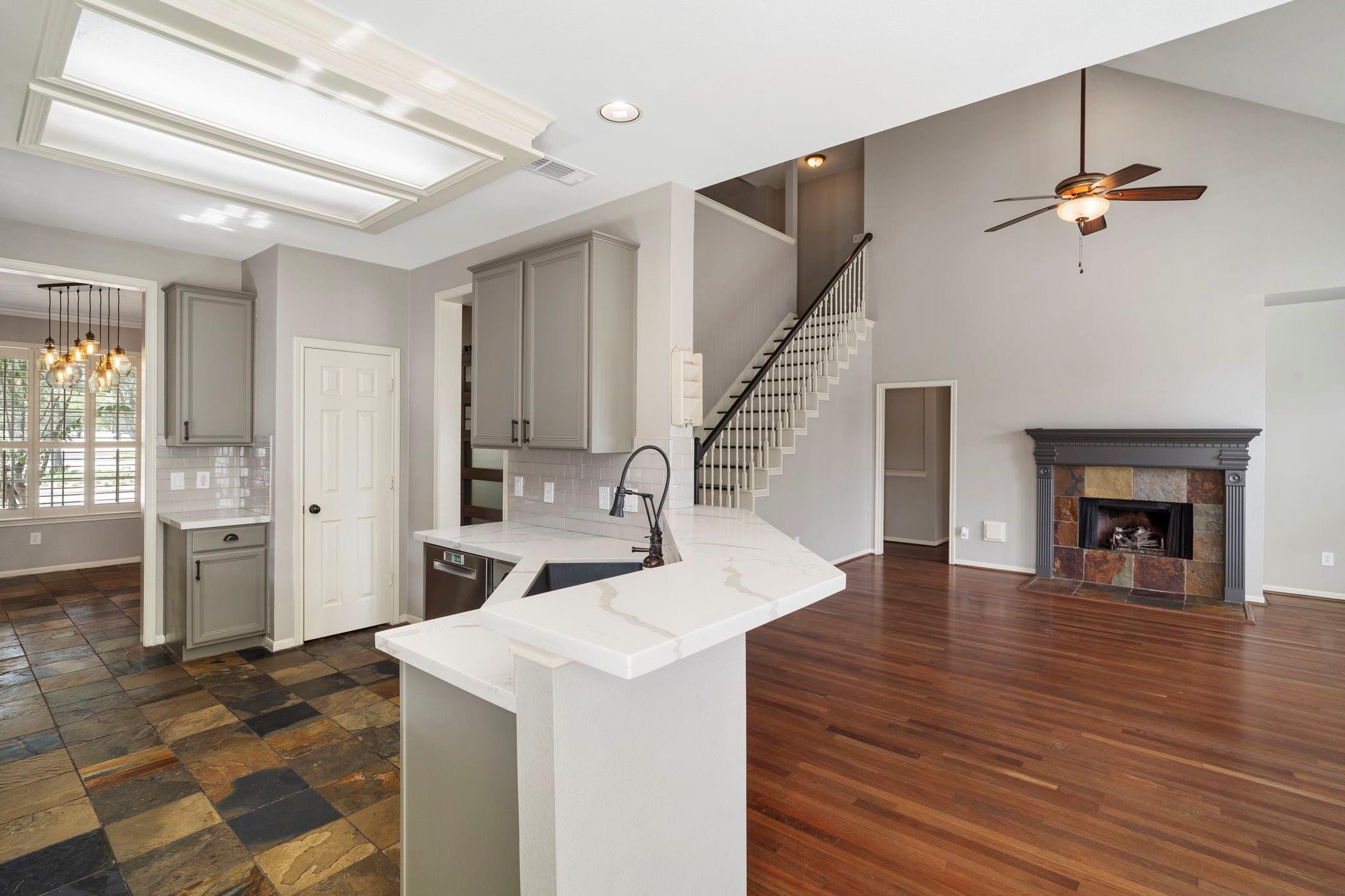 Open-plan kitchen with a large white island, gray cabinets, and an adjoining living area with a stone fireplace.