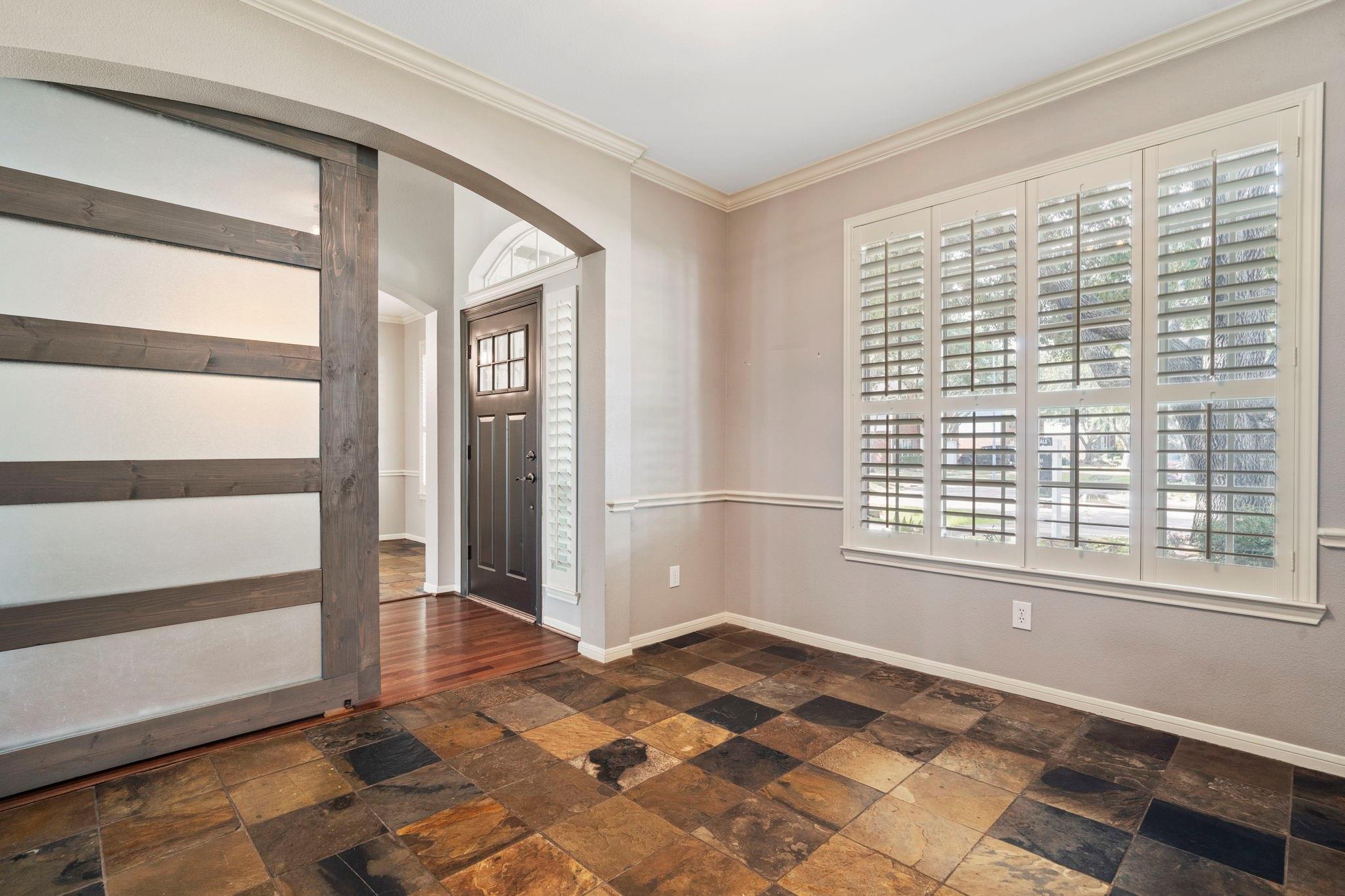 Entryway with multicolored stone tile floors, a sliding barn-style door, and plantation-shuttered windows.
