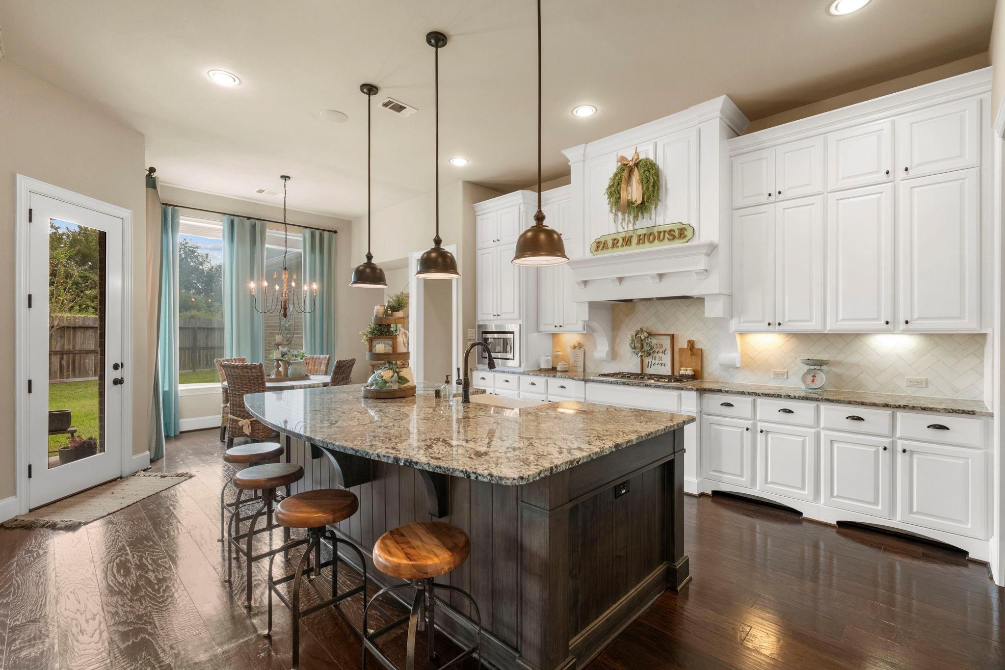 Farmhouse kitchen with a granite-topped island, dark wood stools, and white cabinetry.