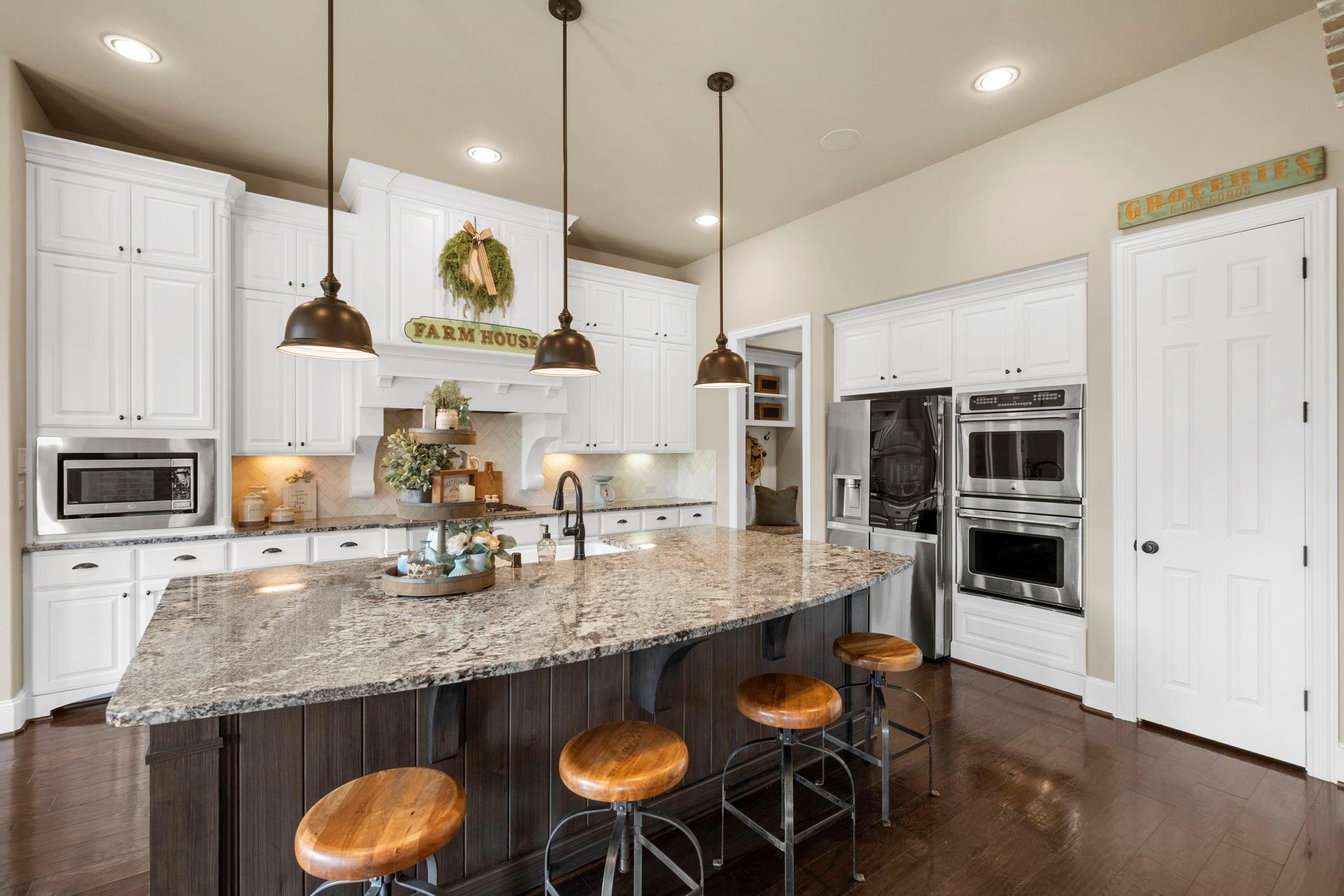Farmhouse kitchen with a large granite island, white cabinetry, and stainless steel appliances.