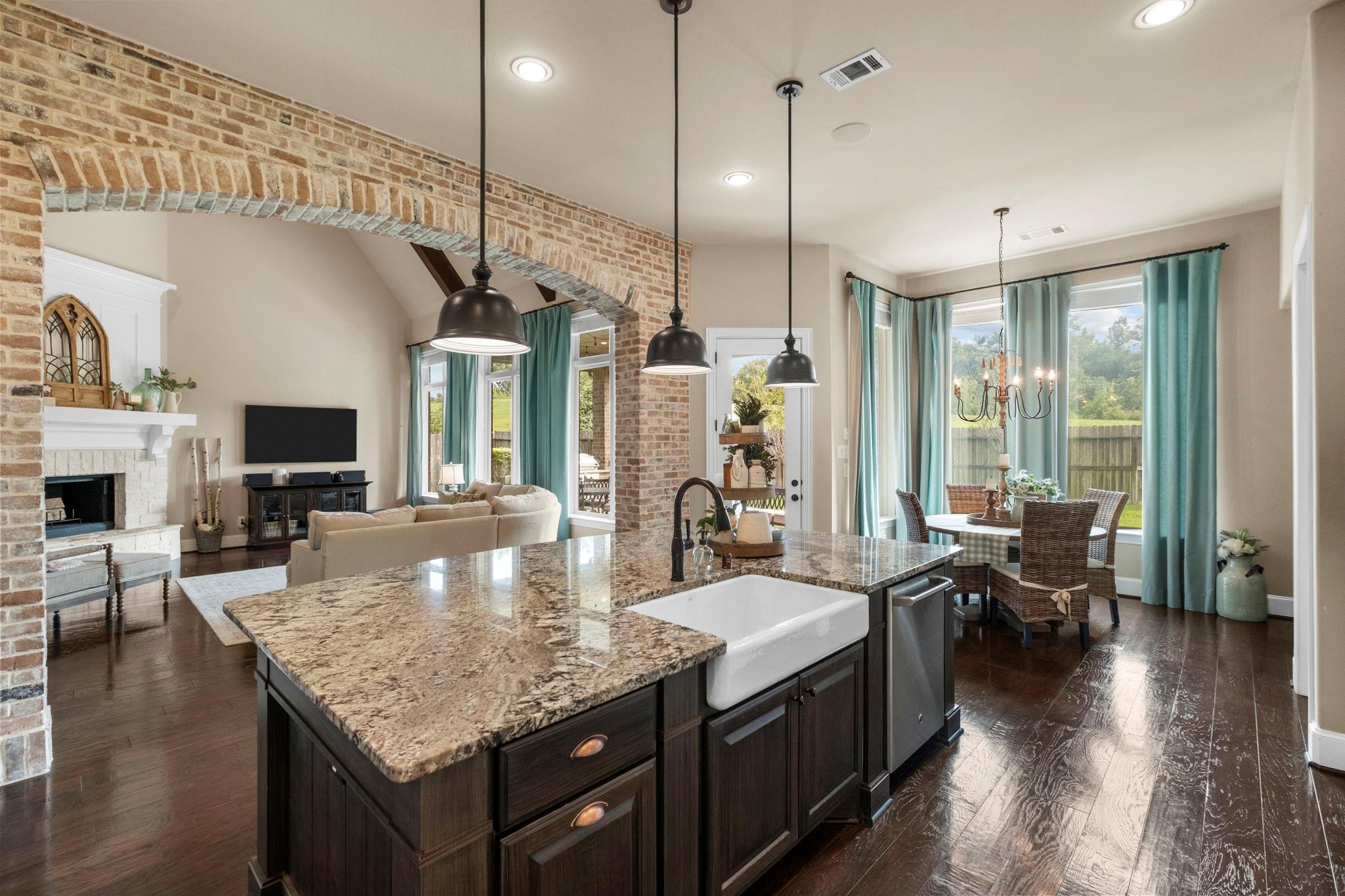 Kitchen with a granite island and farmhouse sink, opening to a living room framed by a brick arch.