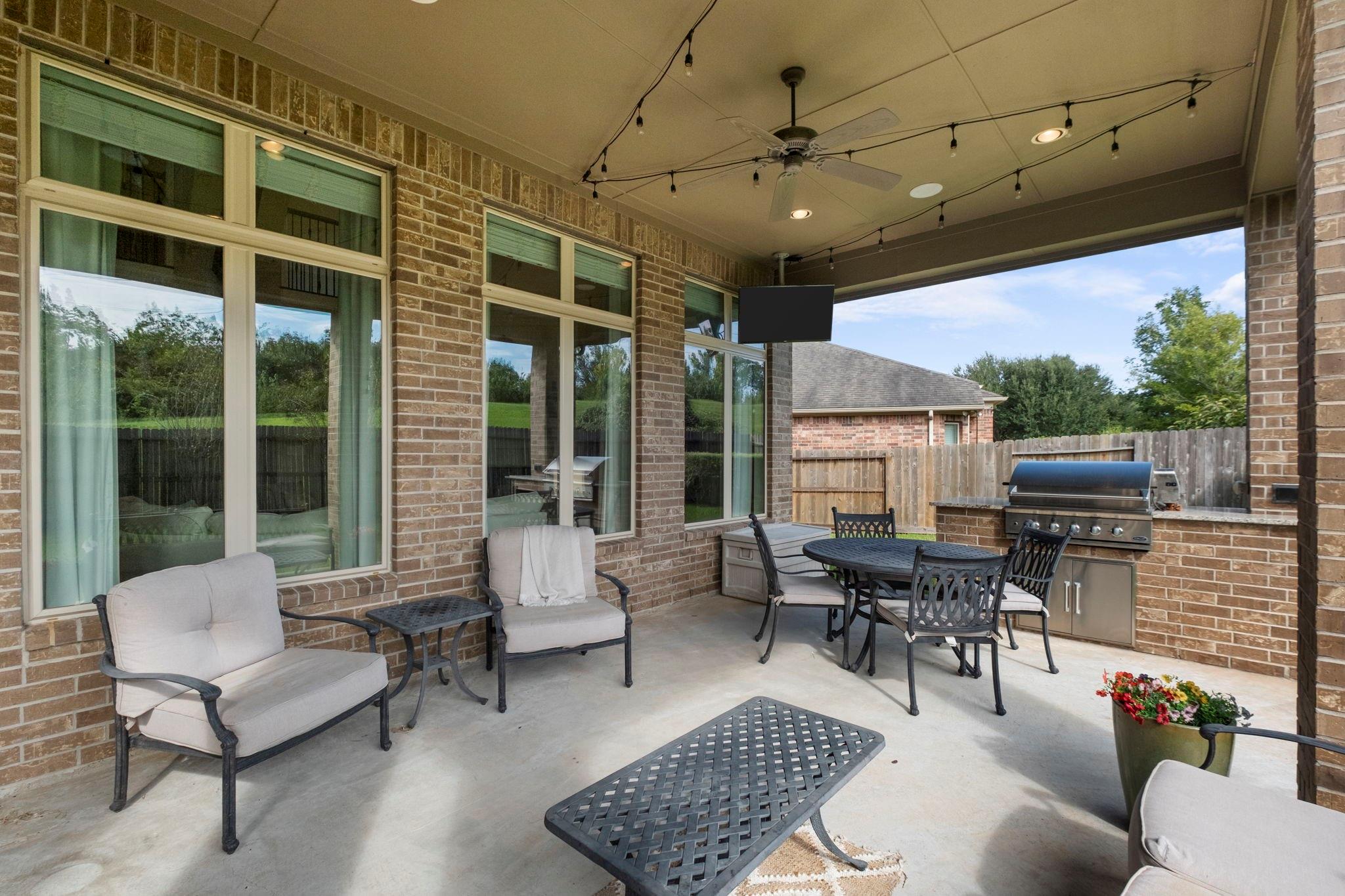 Covered brick patio furnished with lounge chairs and a dining set beside a built-in grill.