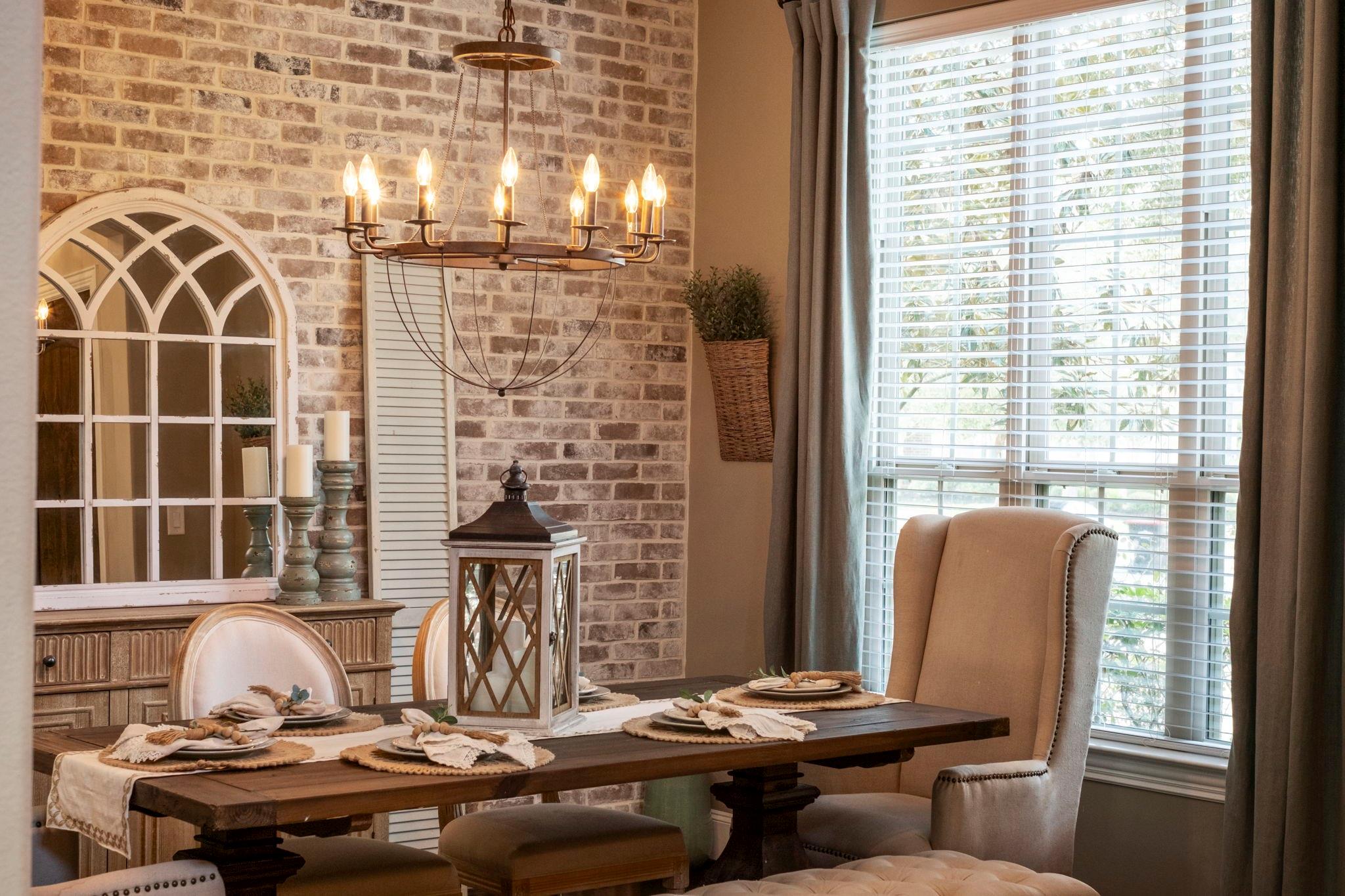 Dining room with a set table, brick accent wall, arched mirror, and chandelier.