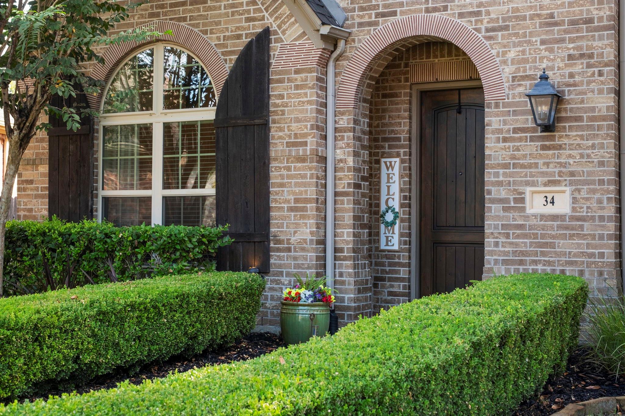 Brick home entrance with an arched doorway, dark wood door, and neatly trimmed hedges.