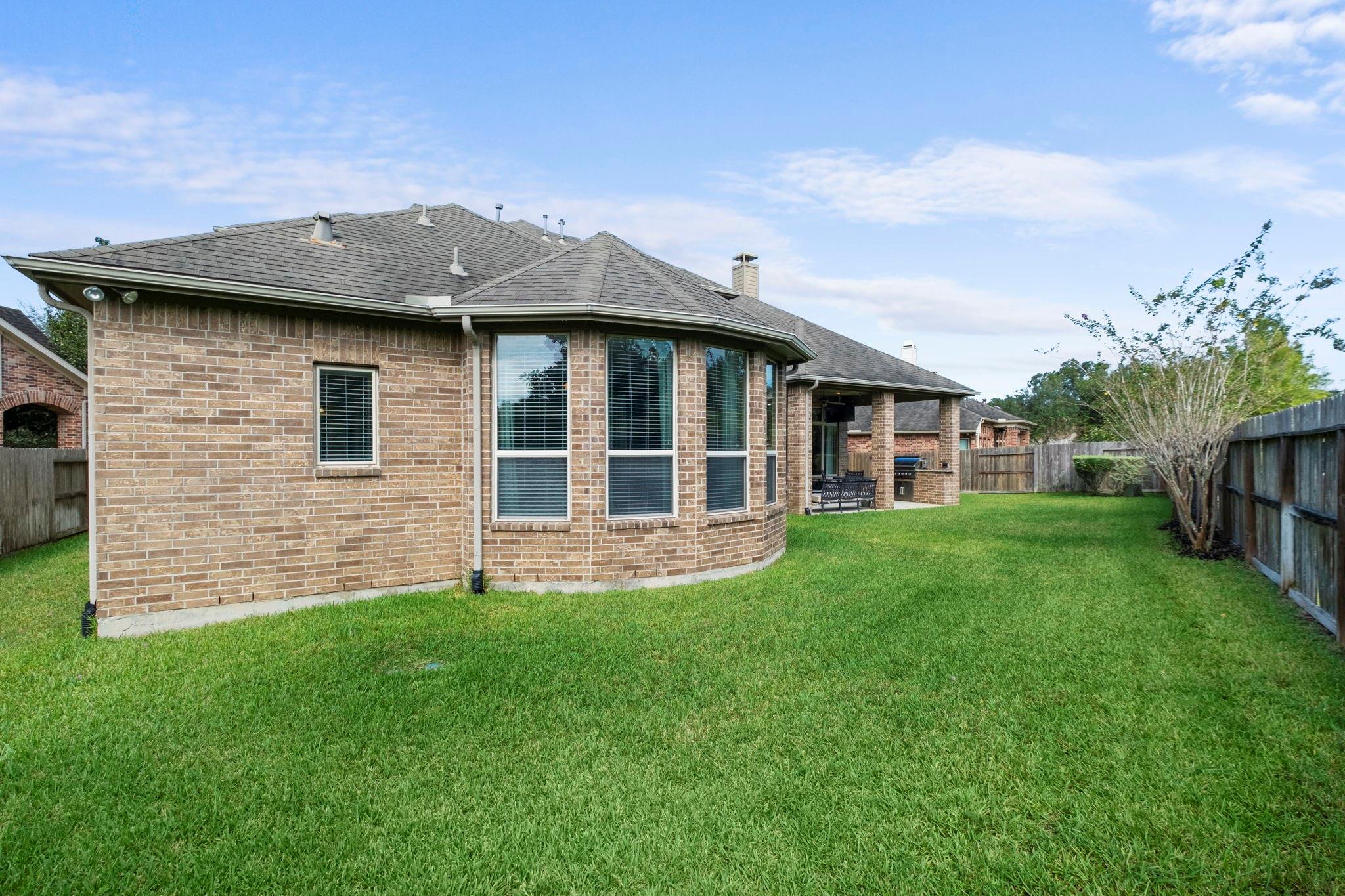 Brick home's rear exterior with bay windows, a covered patio, and a fenced lawn.