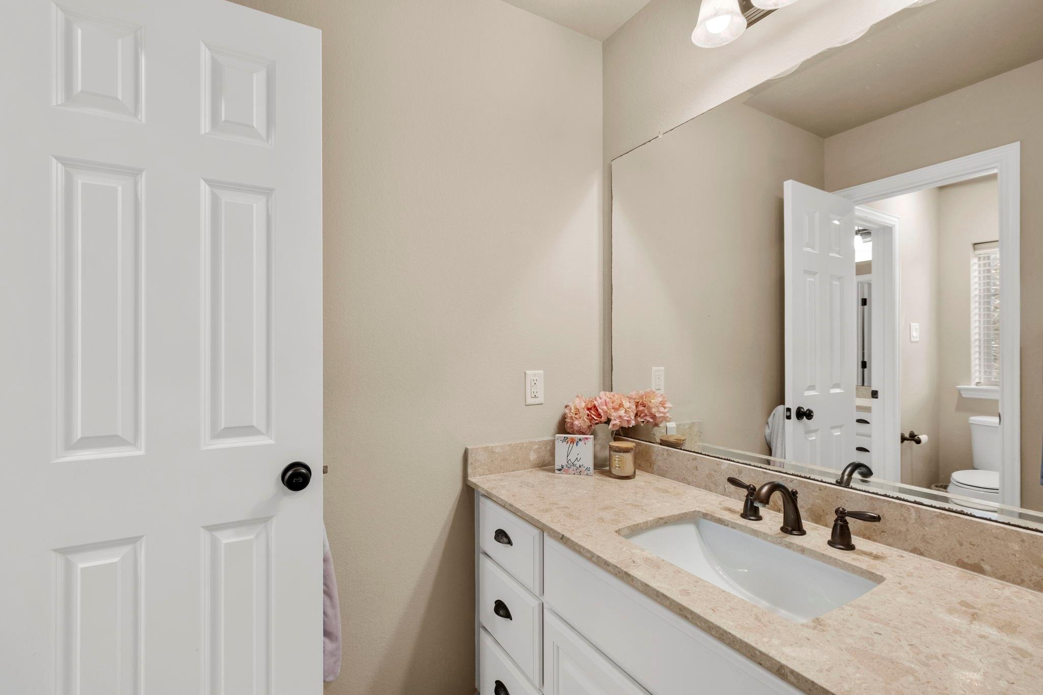 Bathroom vanity with a beige stone counter, undermount sink, and large mirror.