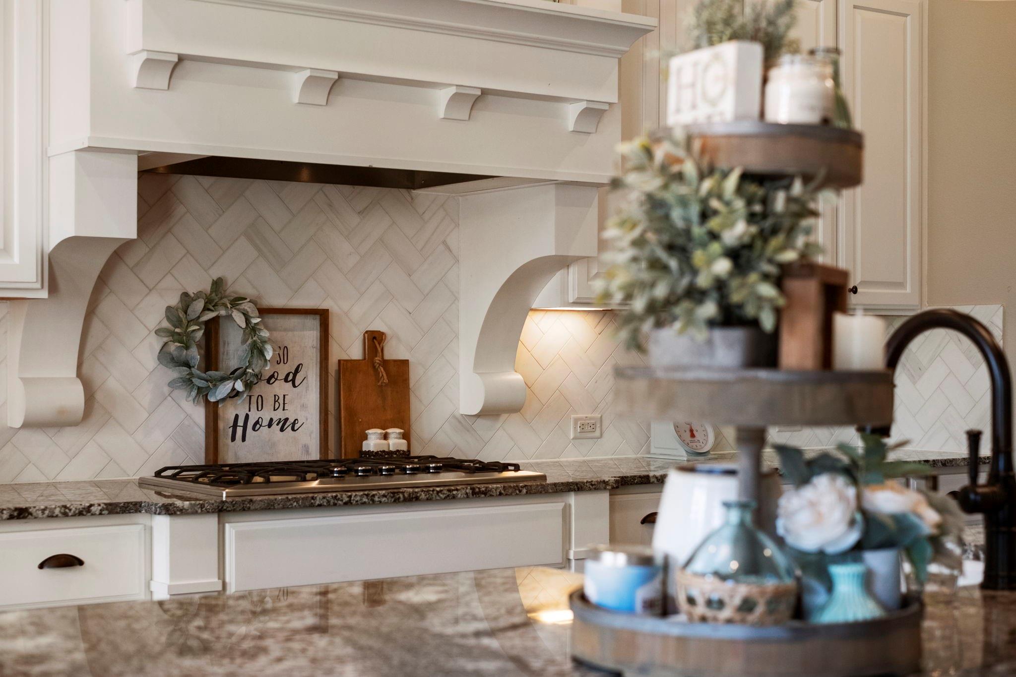 Kitchen with white cabinetry, herringbone tile backsplash, and a gas cooktop beneath a decorative range hood.