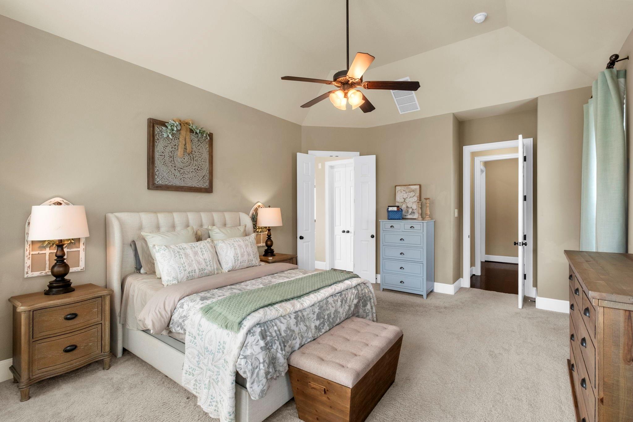 Furnished bedroom with a tufted bed, blue dresser, and vaulted ceiling with ceiling fan.