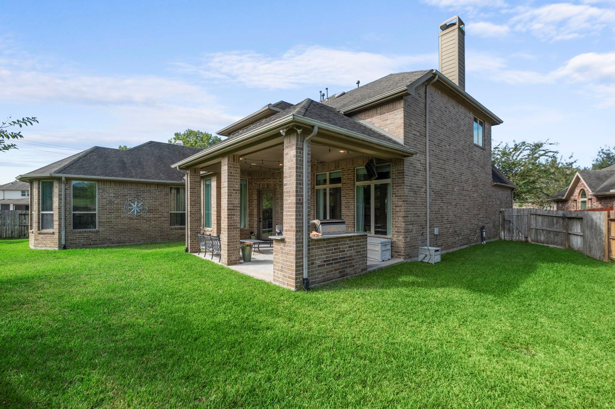 Brick house with a covered patio and outdoor grill overlooking a broad green lawn.