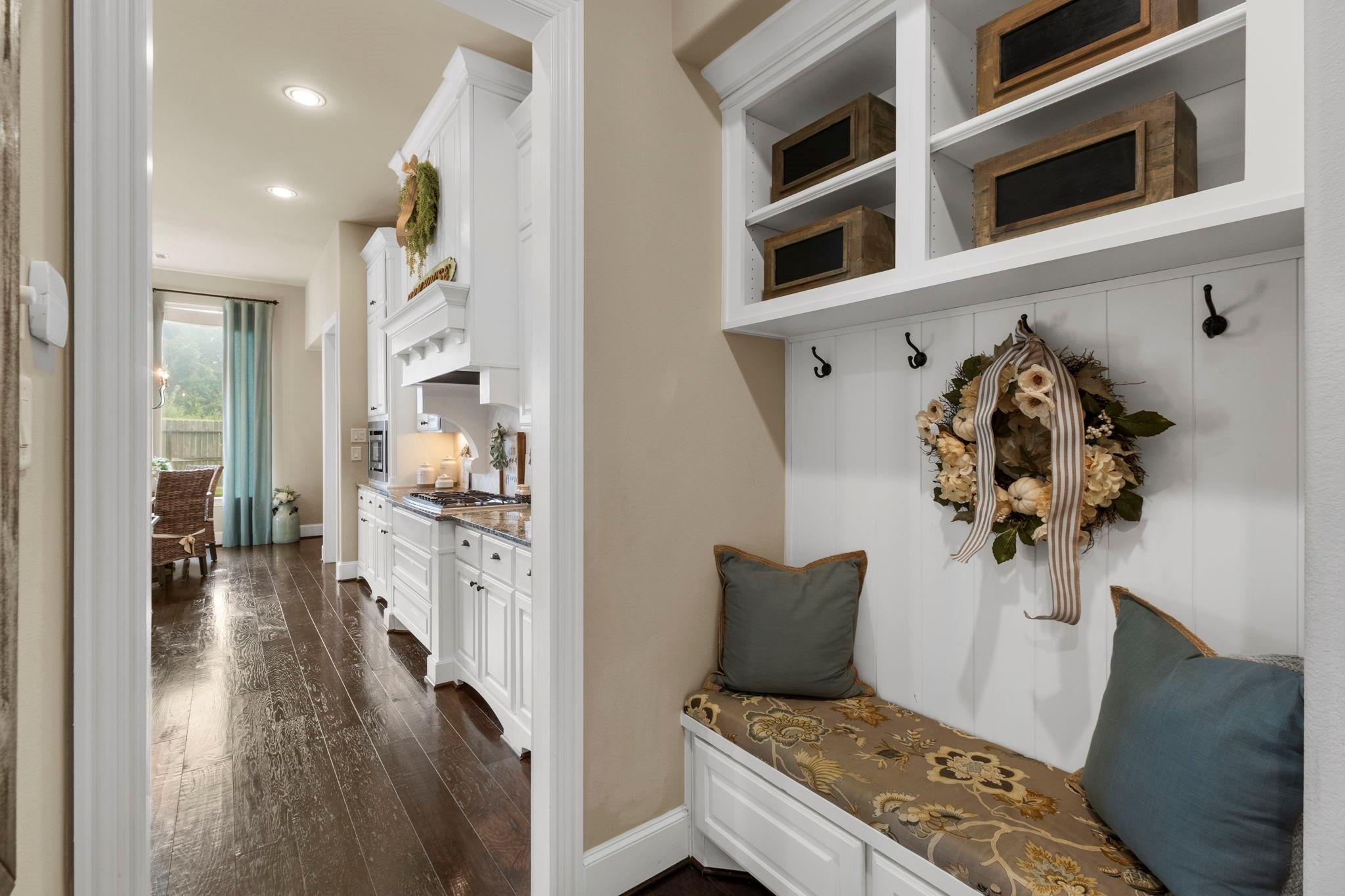 Entry mudroom bench with built-in cubbies and hooks beside a white kitchen with dark wood floors.
