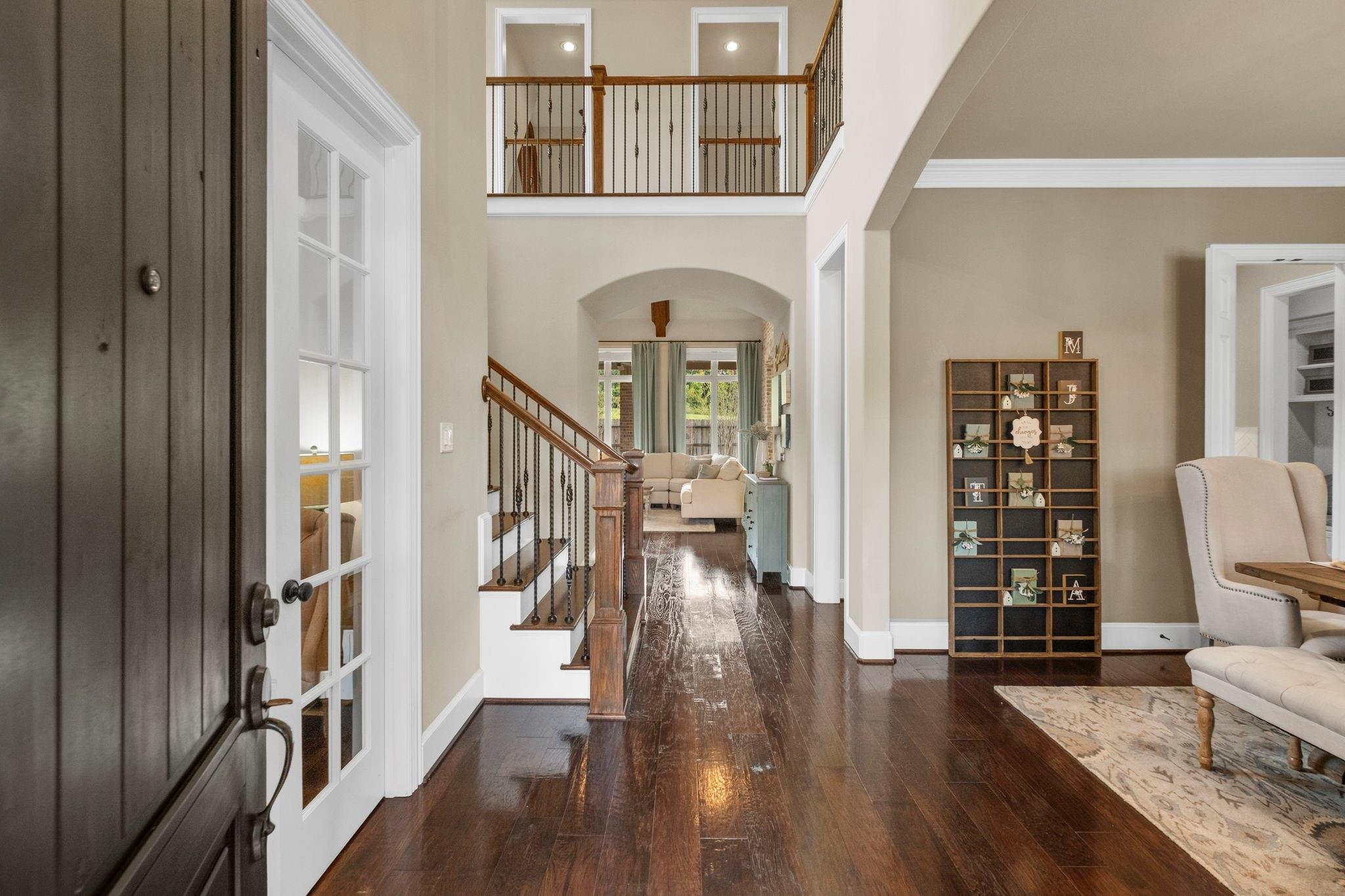 Two-story entry foyer with dark hardwood floors, a wood-and-iron staircase, and an arched opening to a sitting area.