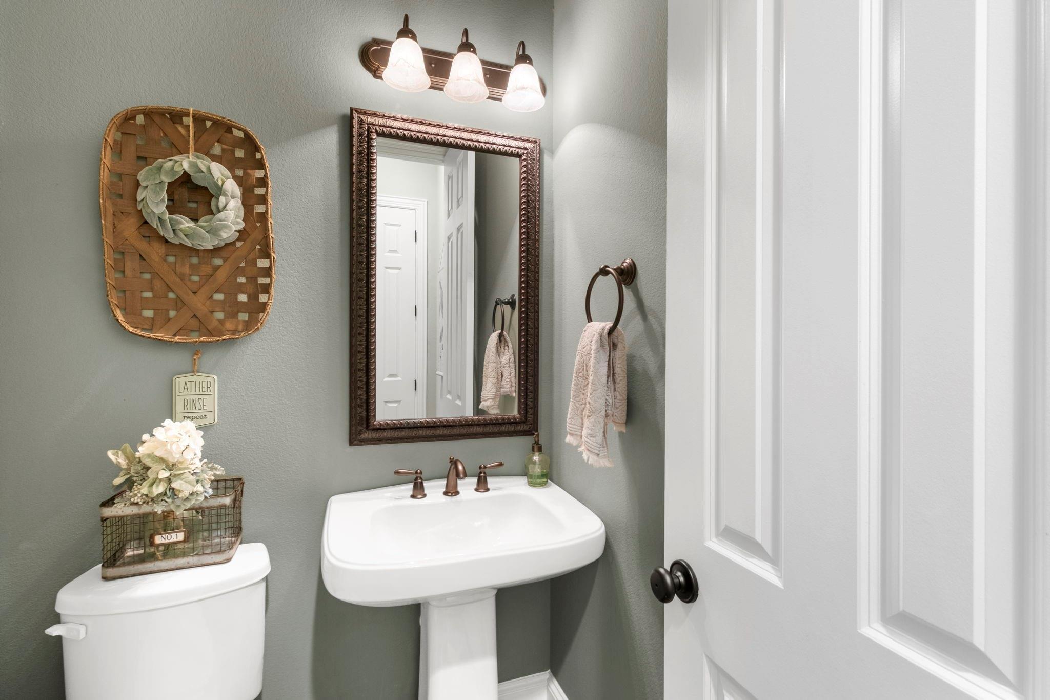 Powder room with a white pedestal sink, toilet, ornate mirror, and bronze fixtures.