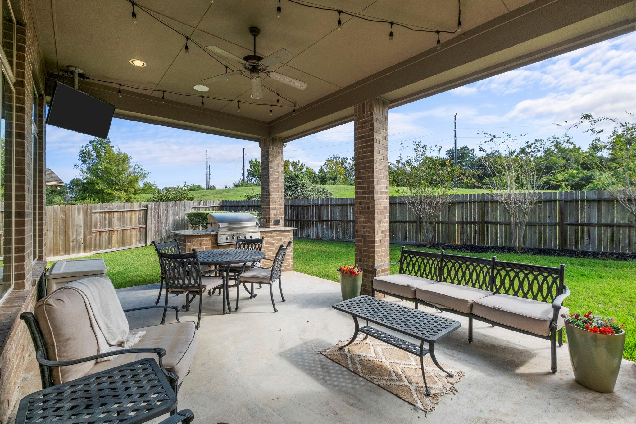 Covered backyard patio with a built-in grill, outdoor dining table, and lounge seating.