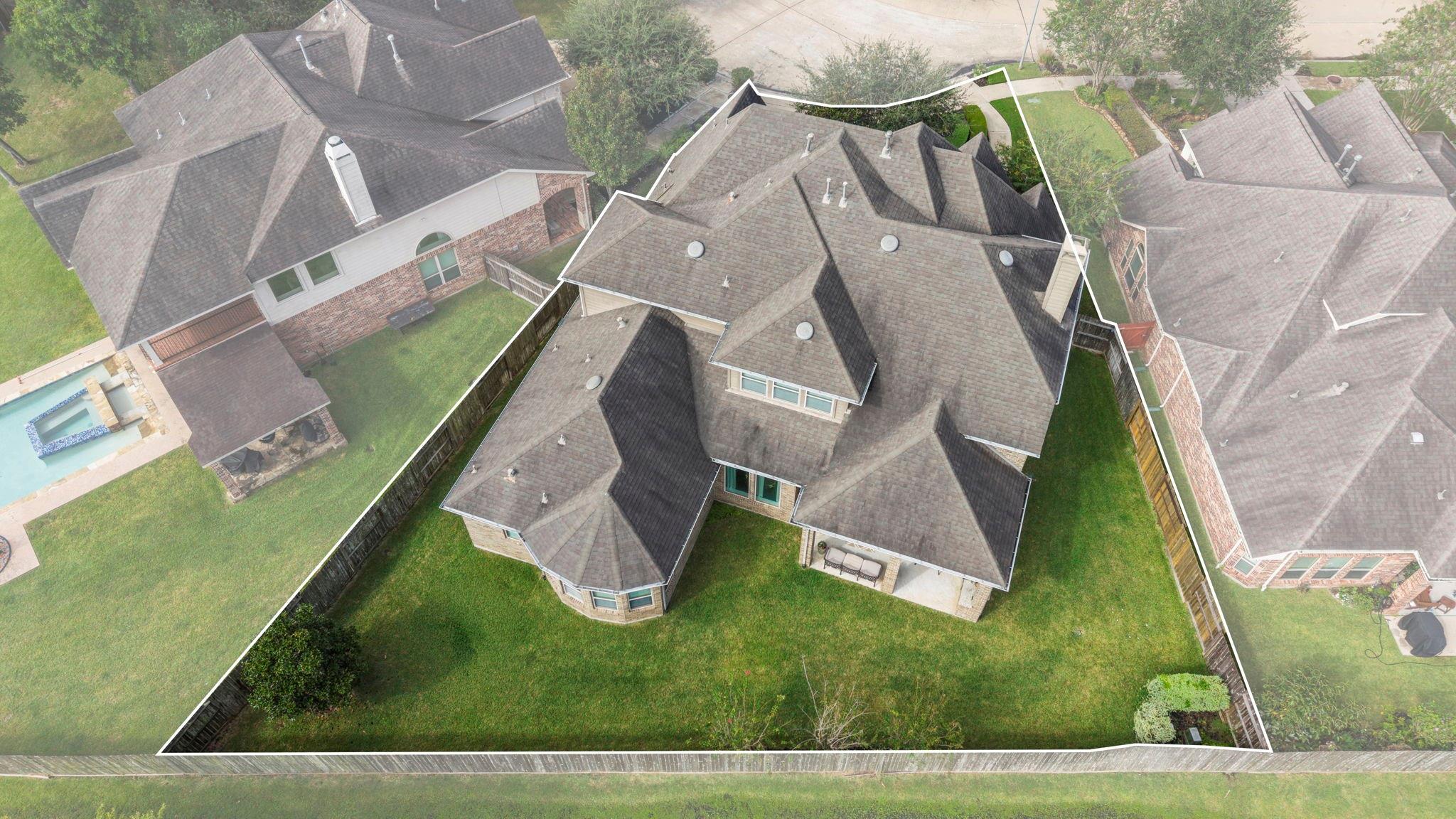 Aerial view of a brick house and fenced lawn, with the property boundary outlined in white.