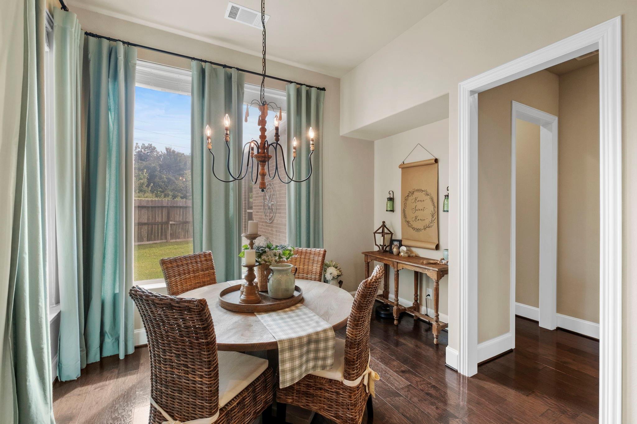 Dining room with wicker chairs, a round table, and tall windows overlooking a fenced backyard.