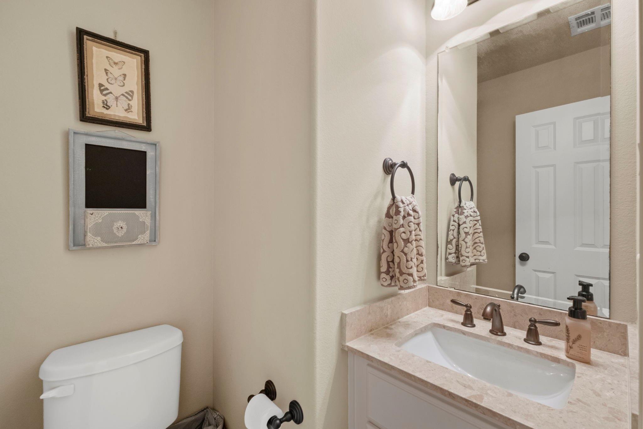Bathroom vanity with stone countertop, large mirror, patterned hand towel, and part of a toilet.