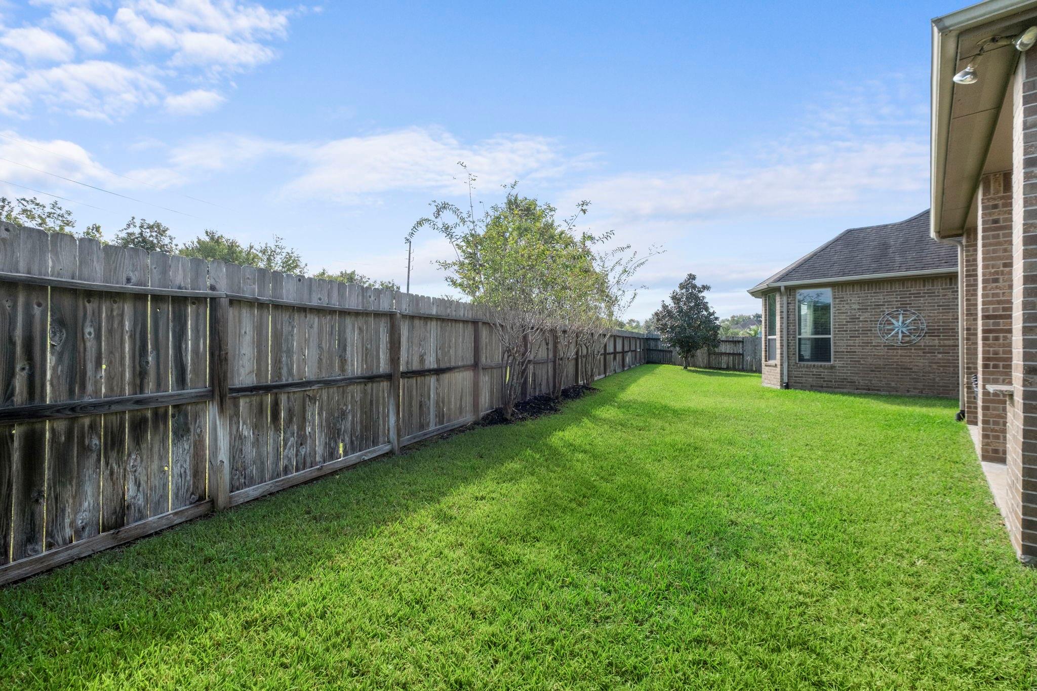 Side yard with a broad green lawn, wooden privacy fence, and brick house exterior.