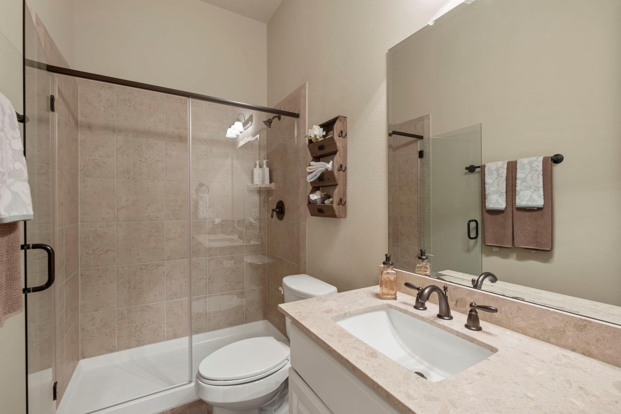 Bathroom with a tiled glass shower, stone vanity, inset sink, and large mirror.