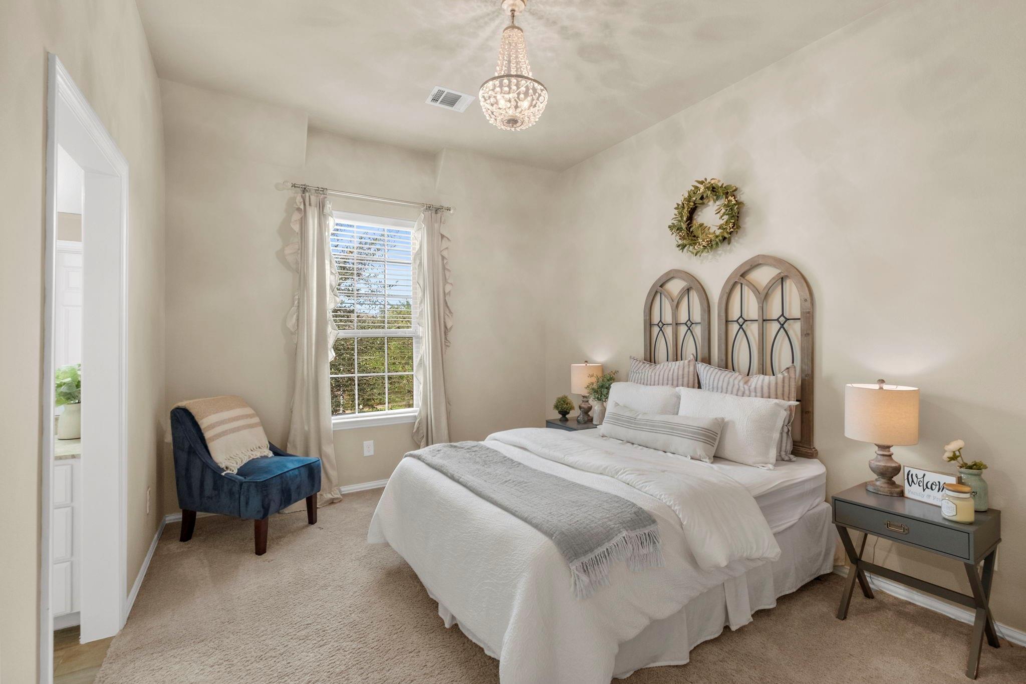 Staged bedroom with a white bed, arched headboard, blue chair, and chandelier.