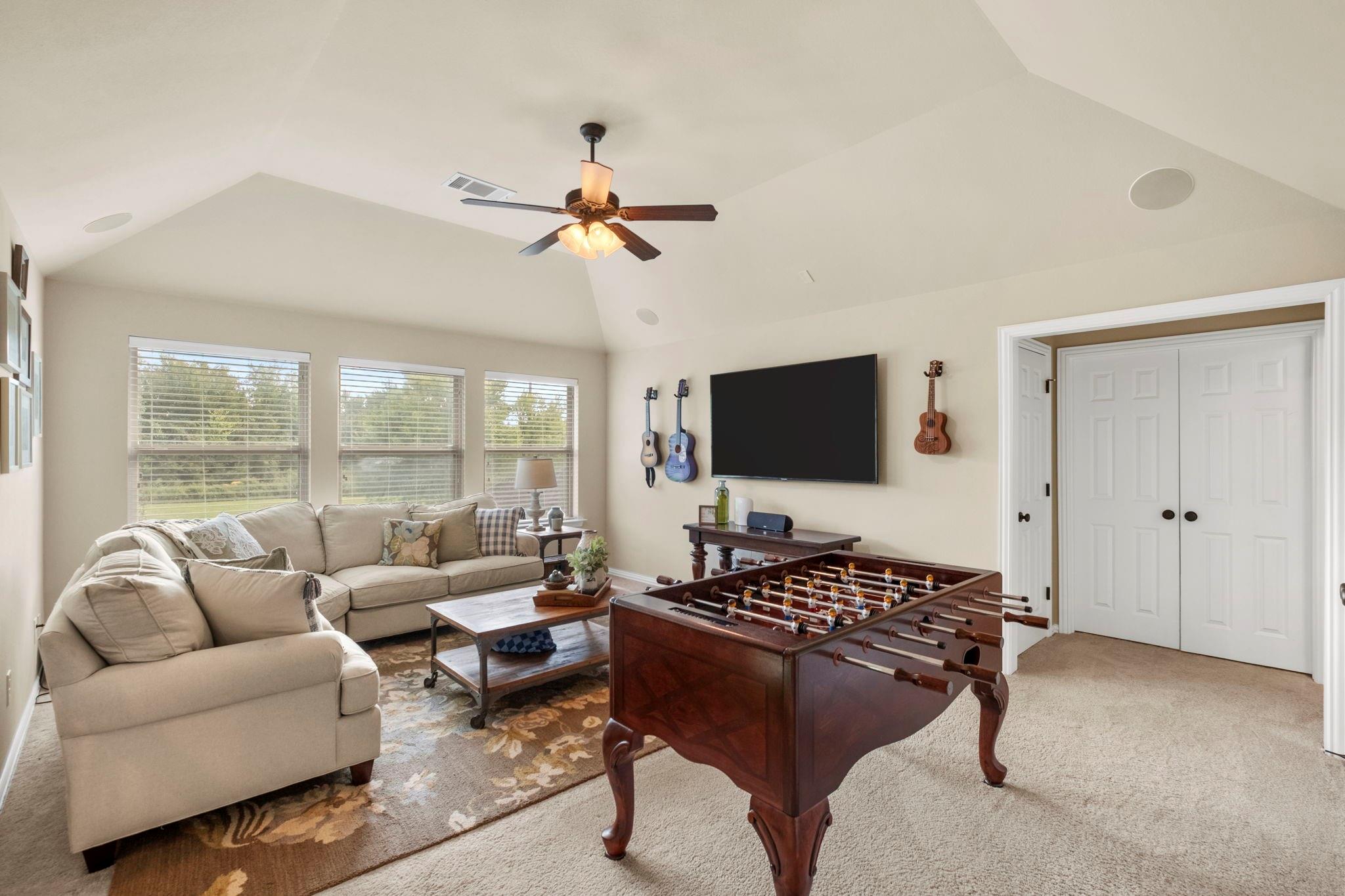 Game room with a foosball table, beige sectional seating, and a wall-mounted television.