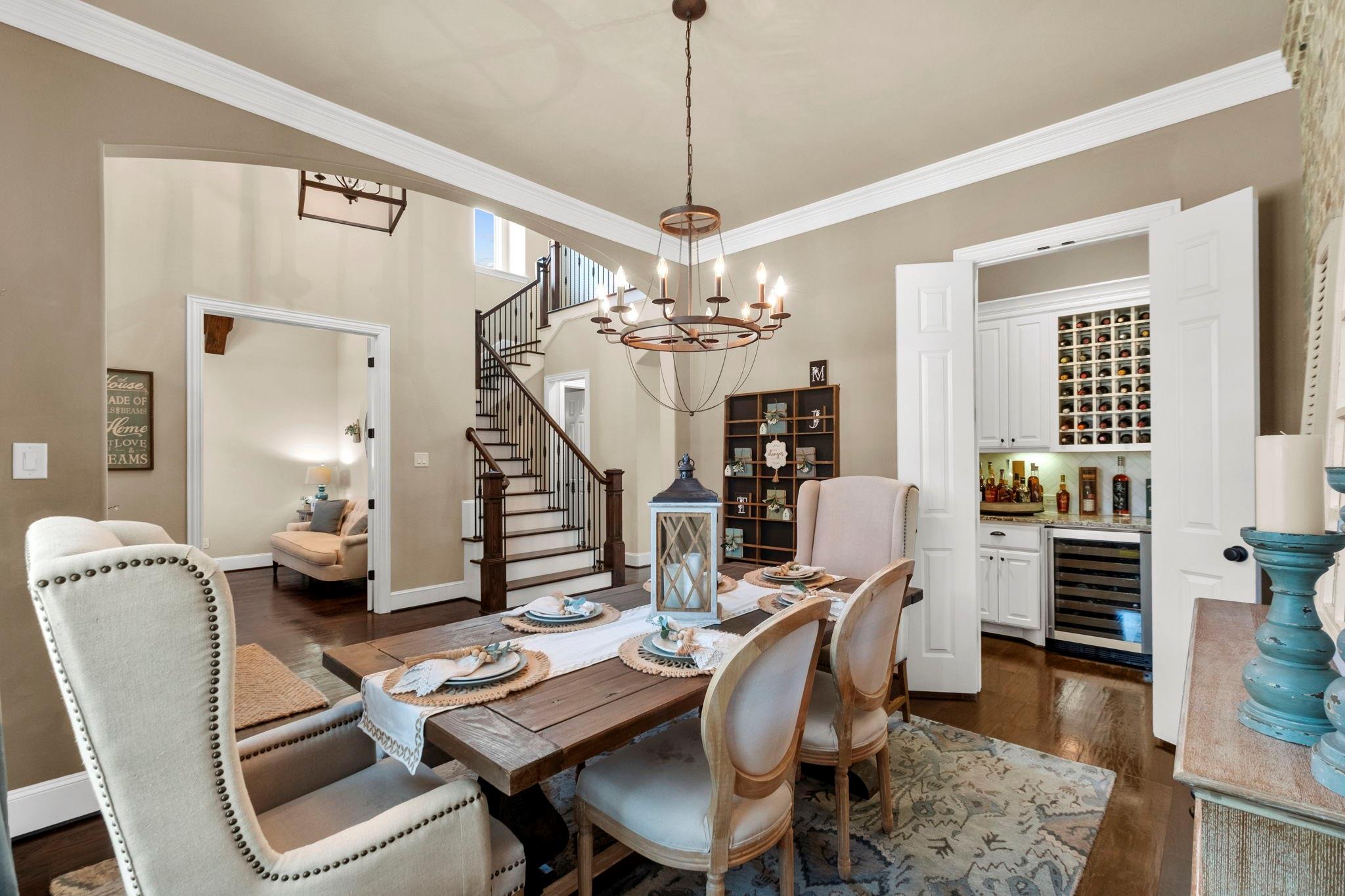 Dining room with a set wooden table, chandelier, staircase, and open doorway to a built-in wine bar.