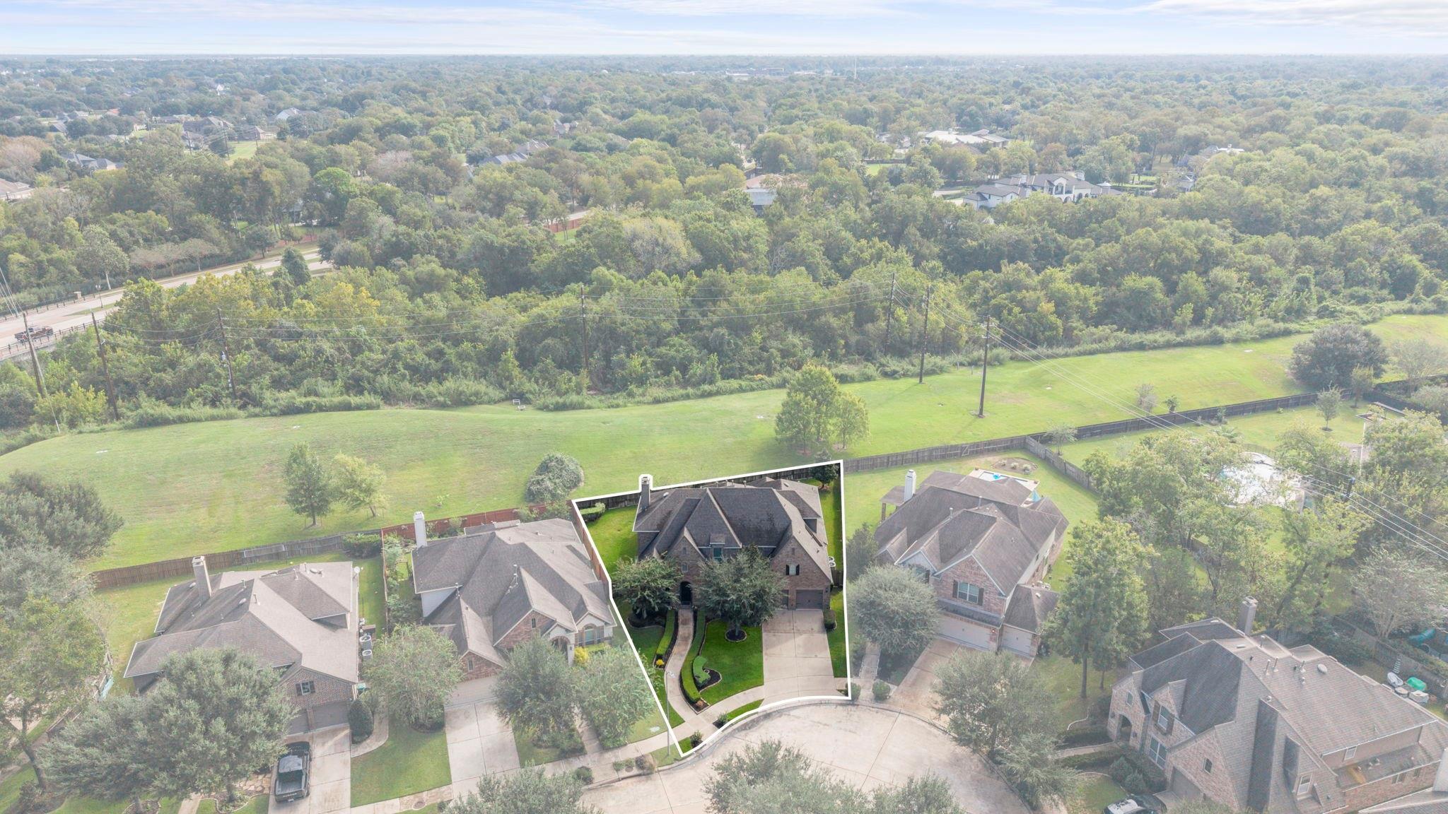 Aerial view of the outlined brick home, with a grassy strip and wooded area behind it.
