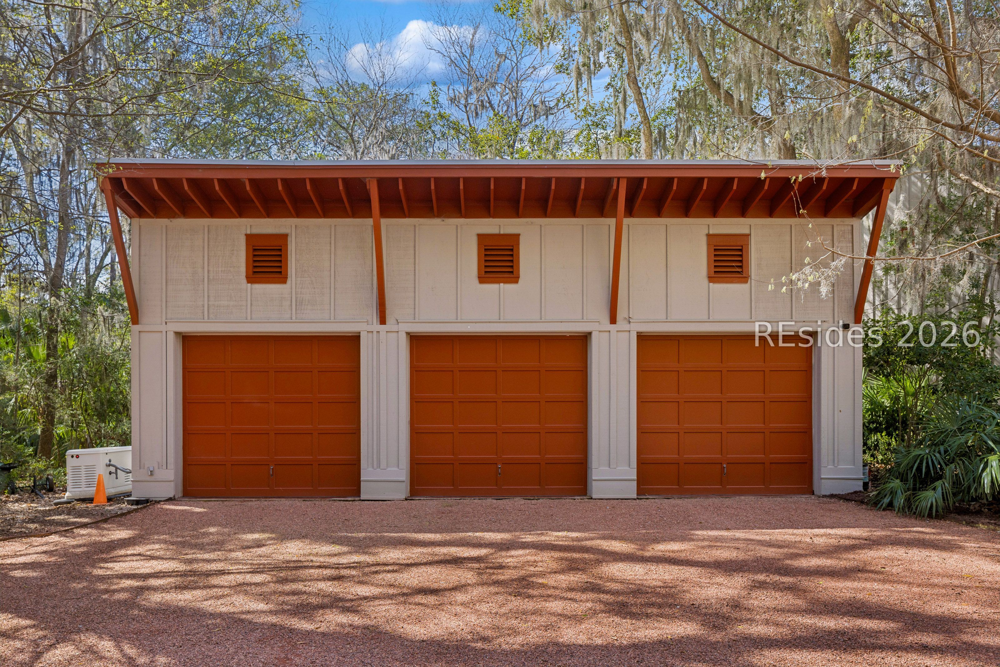 Detached three-bay garage with red-brown doors beneath a broad roof, surrounded by trees.