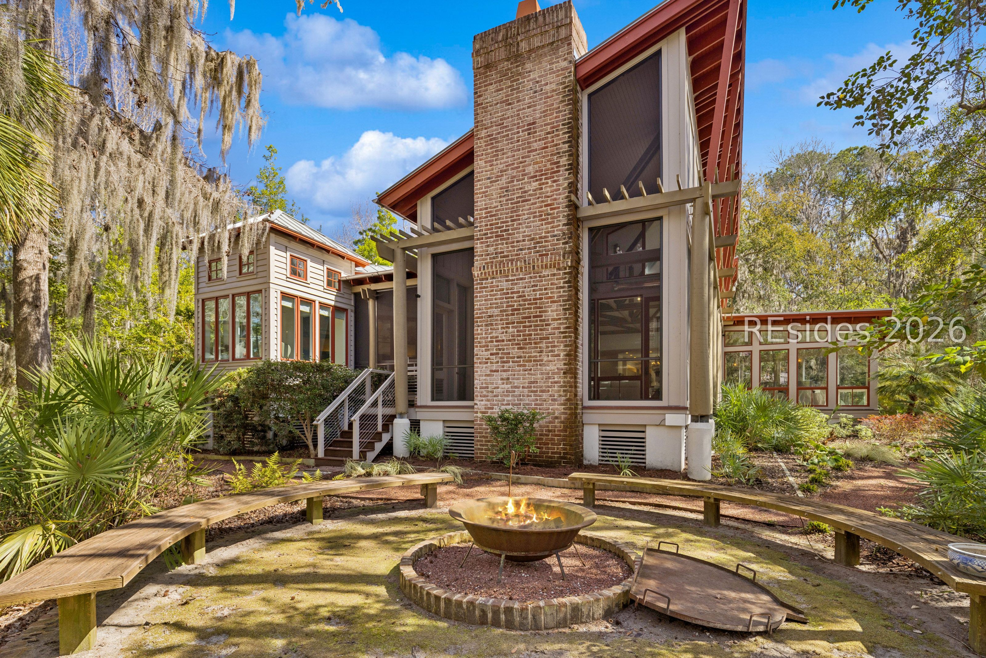Home exterior with a brick chimney and a backyard fire pit surrounded by curved wooden benches.