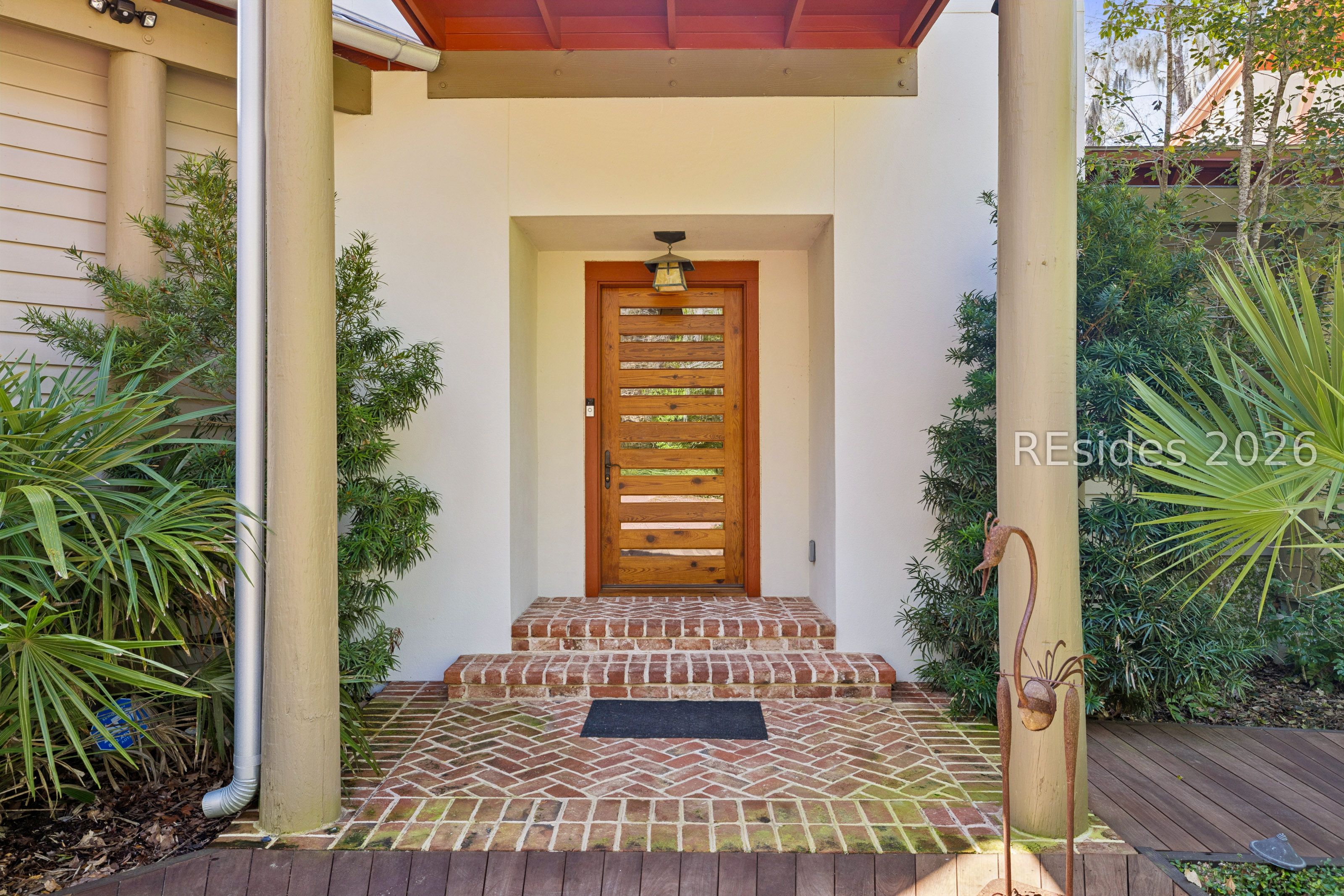 Home entry with a horizontal-slat wooden door, brick steps, and a red porch ceiling.