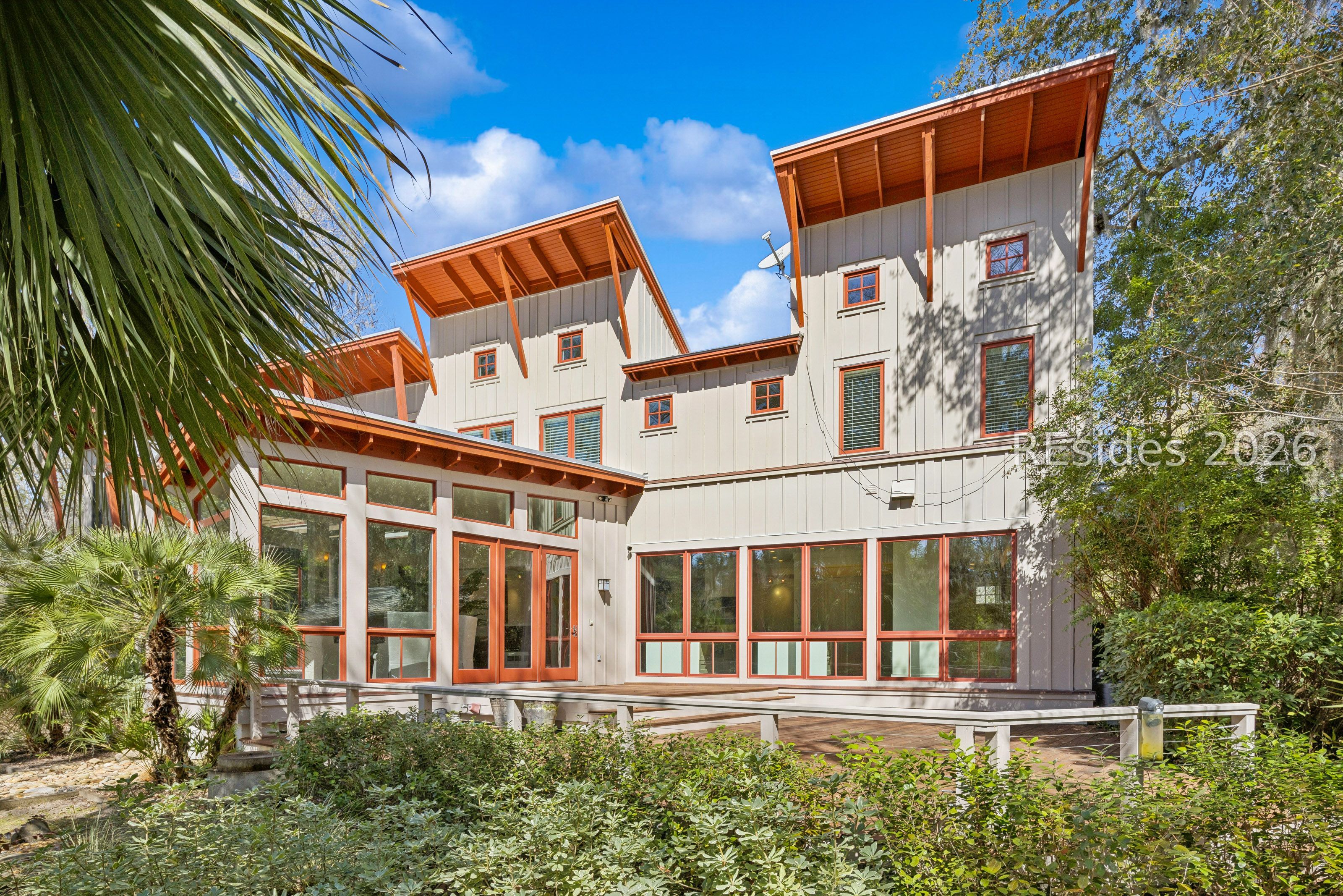 Multi-story home with orange-red trim, tall windows, raised deck, and palm landscaping.