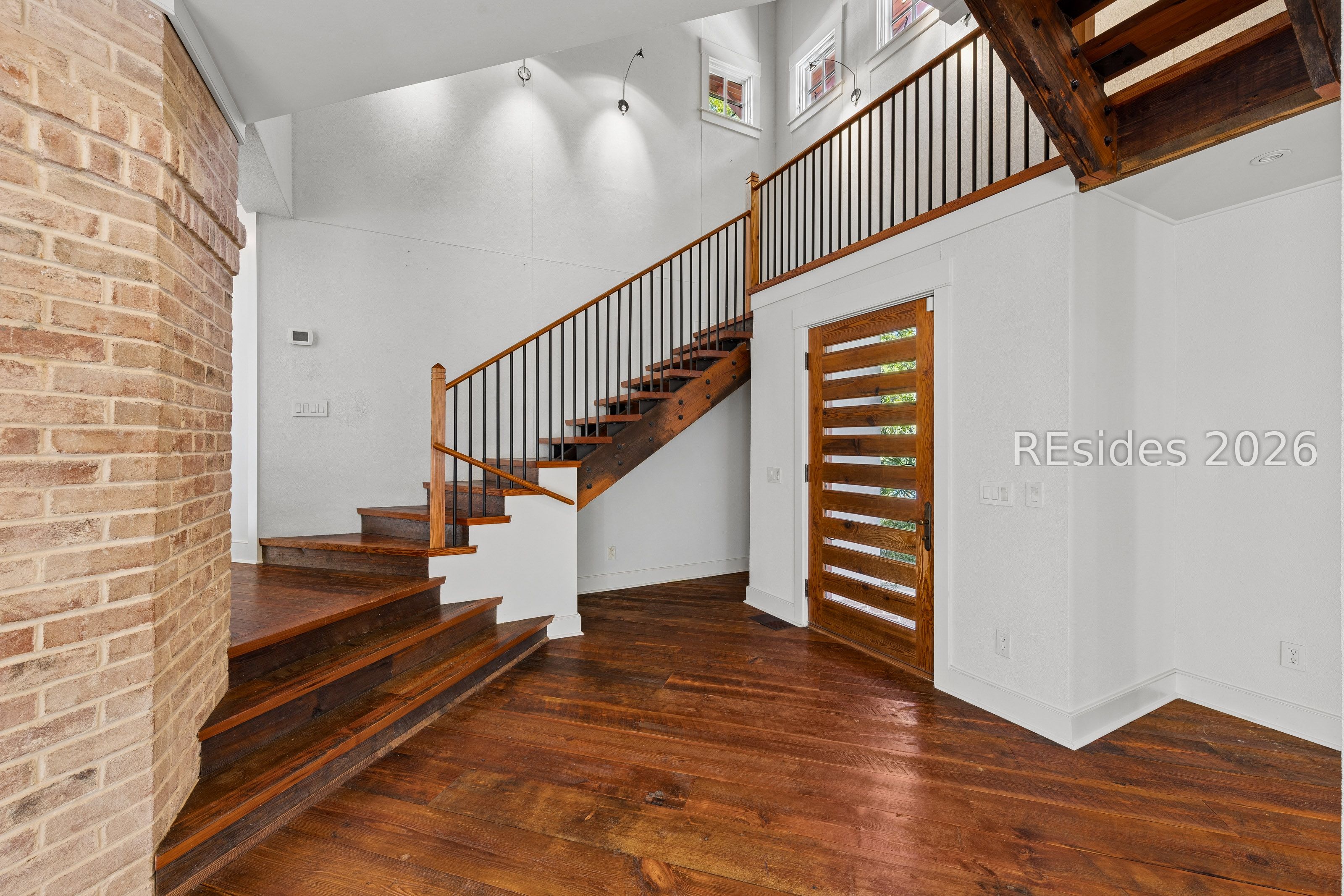 Entry foyer with a wood staircase, exposed beams, brick wall, and slatted wood front door.