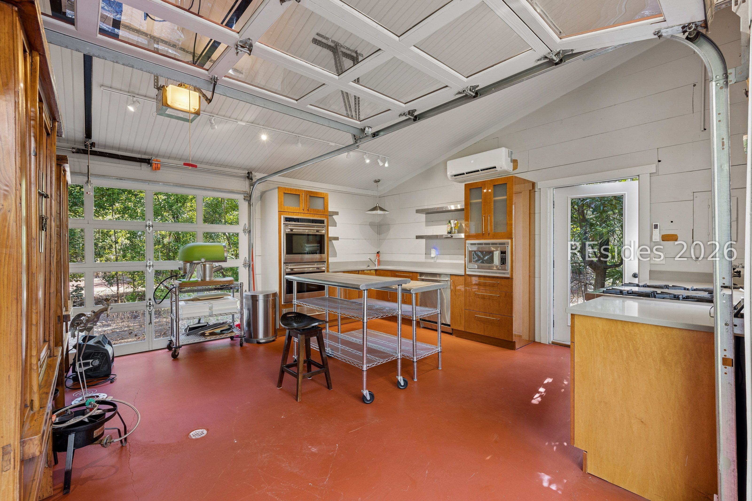 Kitchen in a garage with warm wood cabinets, stainless appliances, and a glass-paneled overhead door.