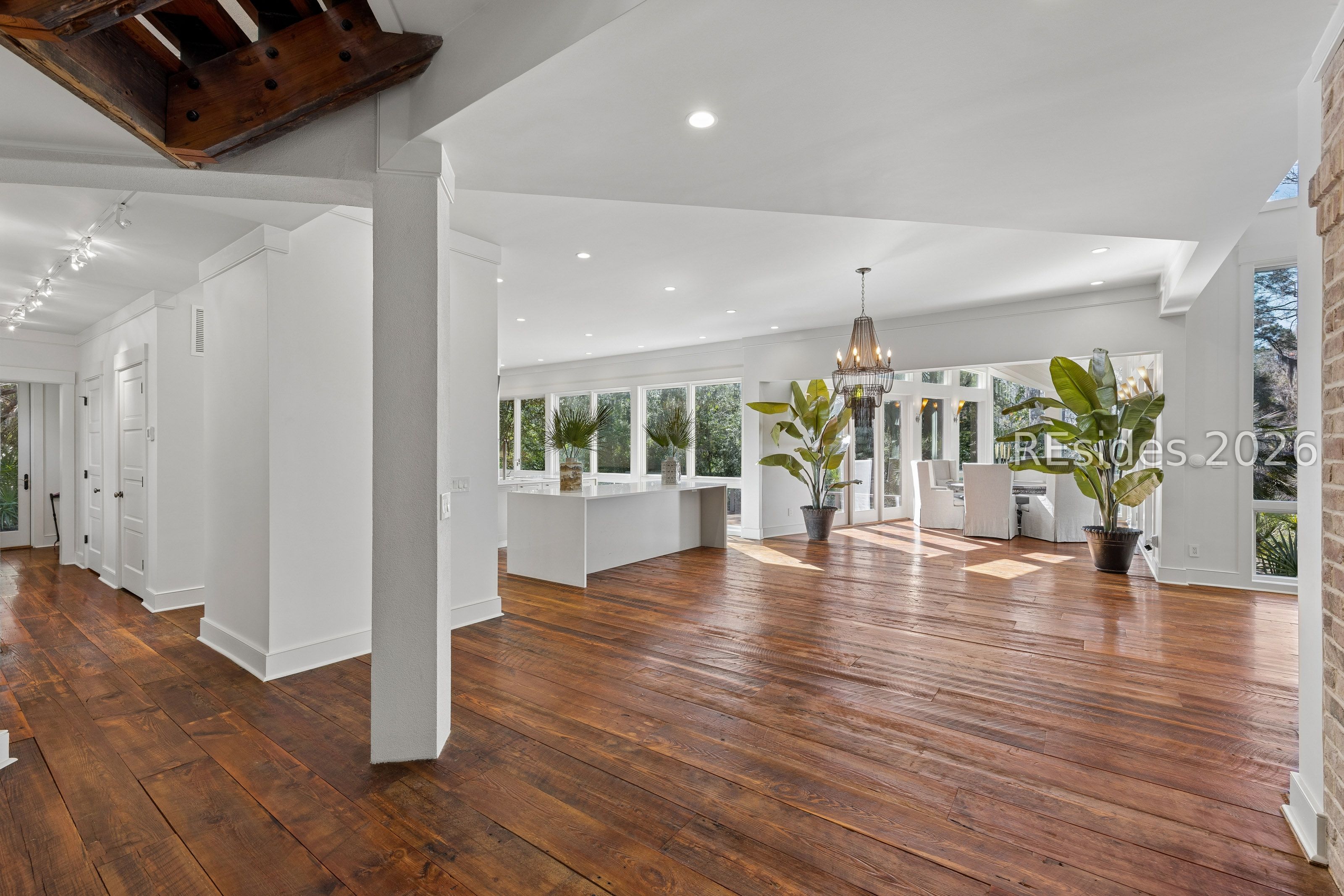 Open kitchen and dining area with wide-plank wood floors, tall windows, and exposed timber beams.