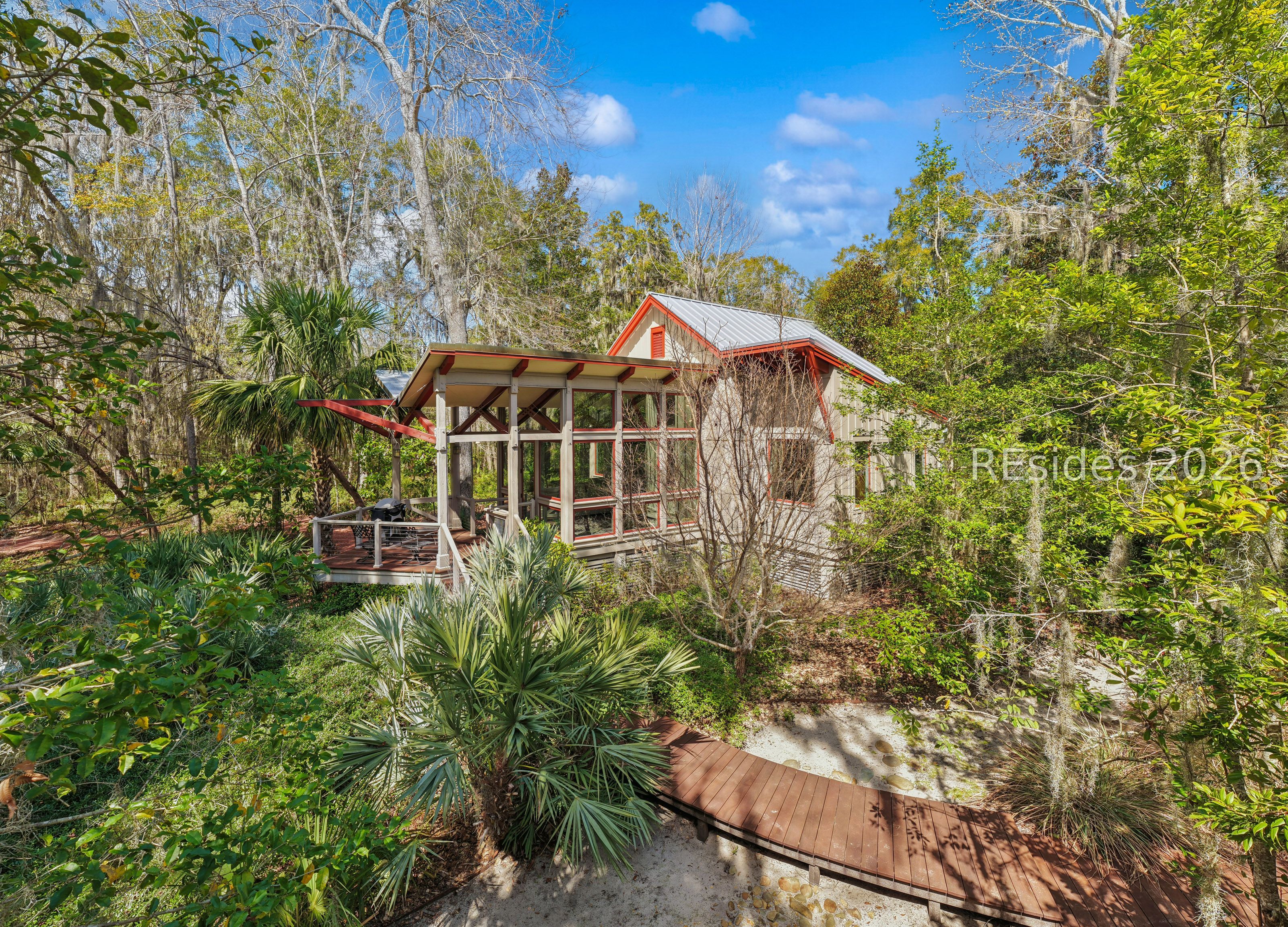 Modern home with red trim, an open deck, and a curved wooden walkway amid dense greenery.