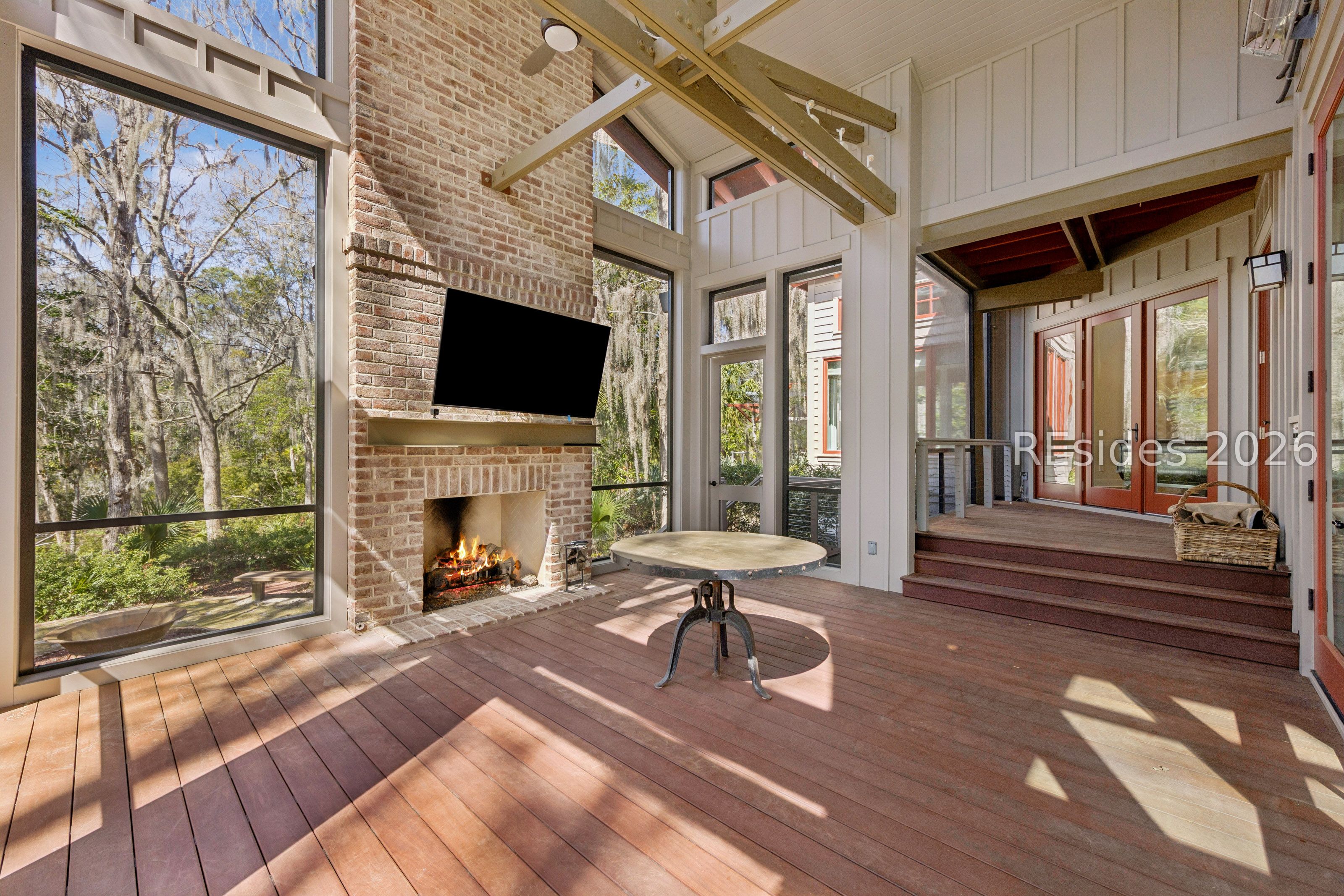 Enclosed sunroom with a brick fireplace, tall windows overlooking trees, and a round table.