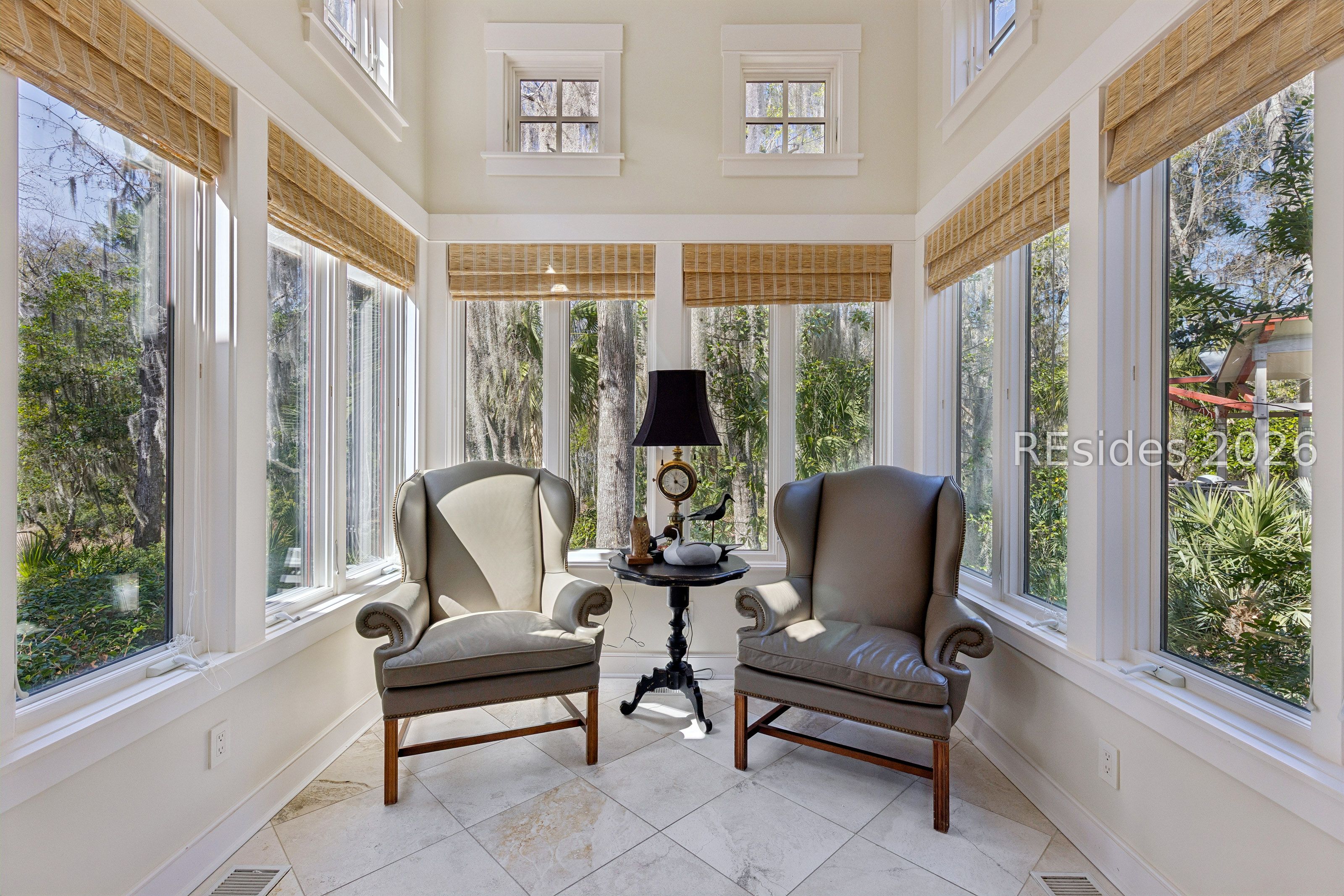 Furnished sunroom with two armchairs and tall windows overlooking trees.