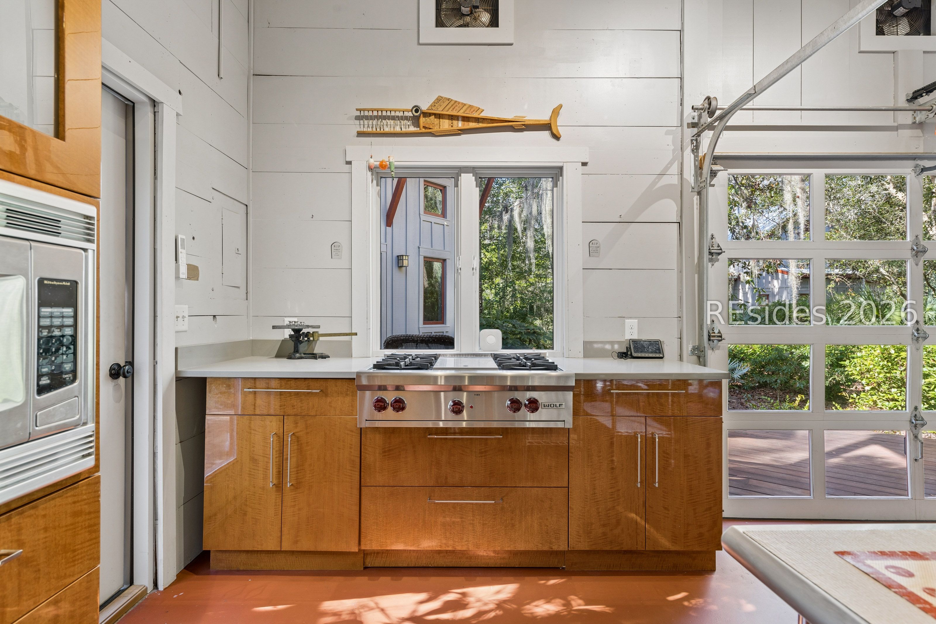 Kitchen with a stainless-steel Wolf range, glossy wood cabinetry, and a glass-paneled garage door.